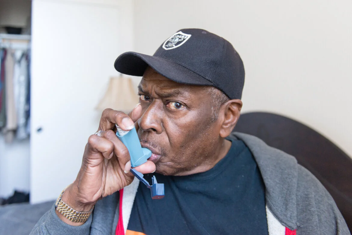 James Lockett, 70, uses his inhaler at his apartment in Oakland. Lockett, who suffers from asthma, says he never leaves home without his inhaler. “If I find I left my inhaler at home, I’m coming back for it,” he said. (Heidi de Marco/California Heal…