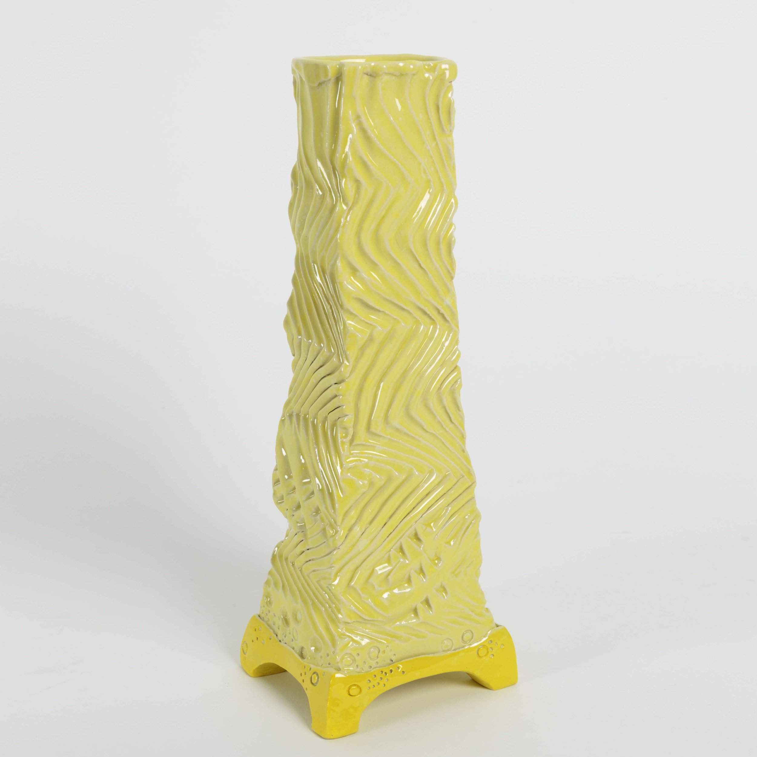 Tall hand-built ceramic vessel with four feet, square tapered form, rhythmic surface texture, and soft yellow and white glaze with a bright yellow base.