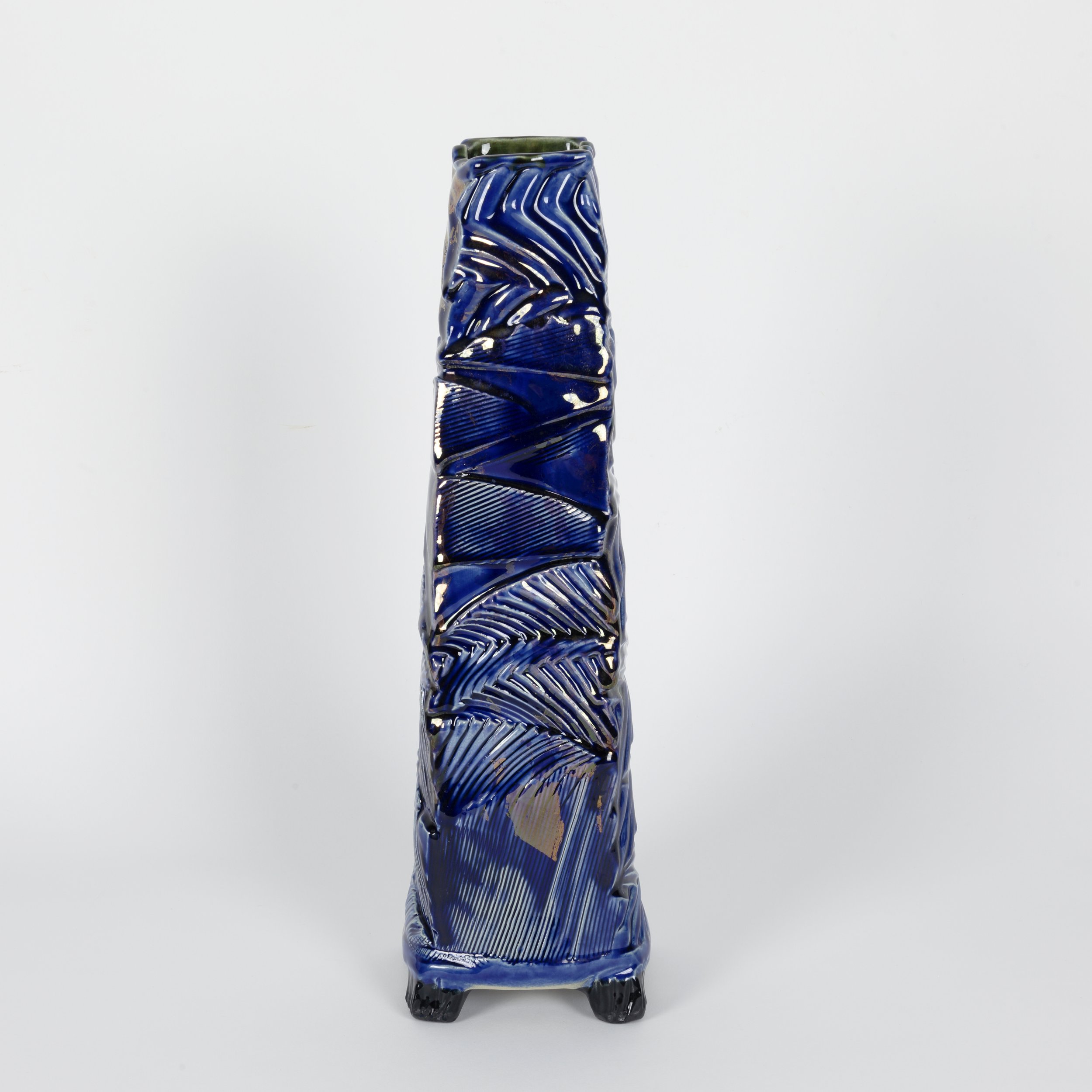 Tall hand-built ceramic vessel with four feet, a square tapered form, rhythmic surface texture, deep blue glazes with layered gold lustre, and a black interior and textured black feet.