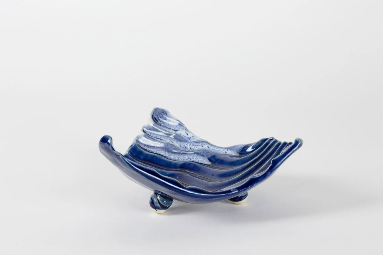 Asymmetric ripple-textured ceramic dish elevated on three rounded feet, finished in a deep blue gloss glaze with a small area of white.