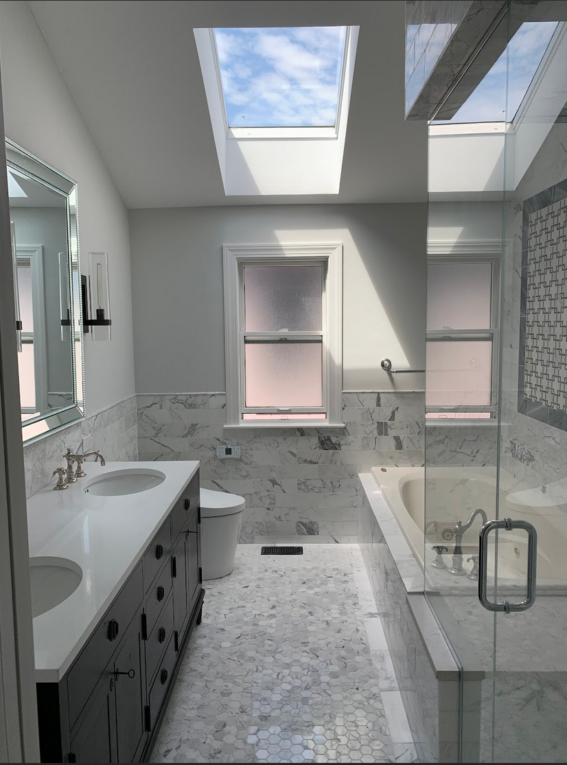Modern bathroom with skylights, double sink vanity, toilet, bathtub, and marble tiles