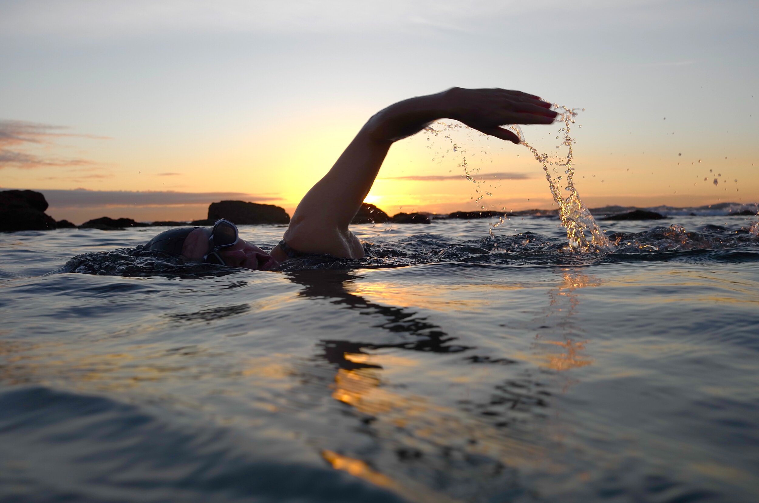 A person swims in the ocean at sunrise