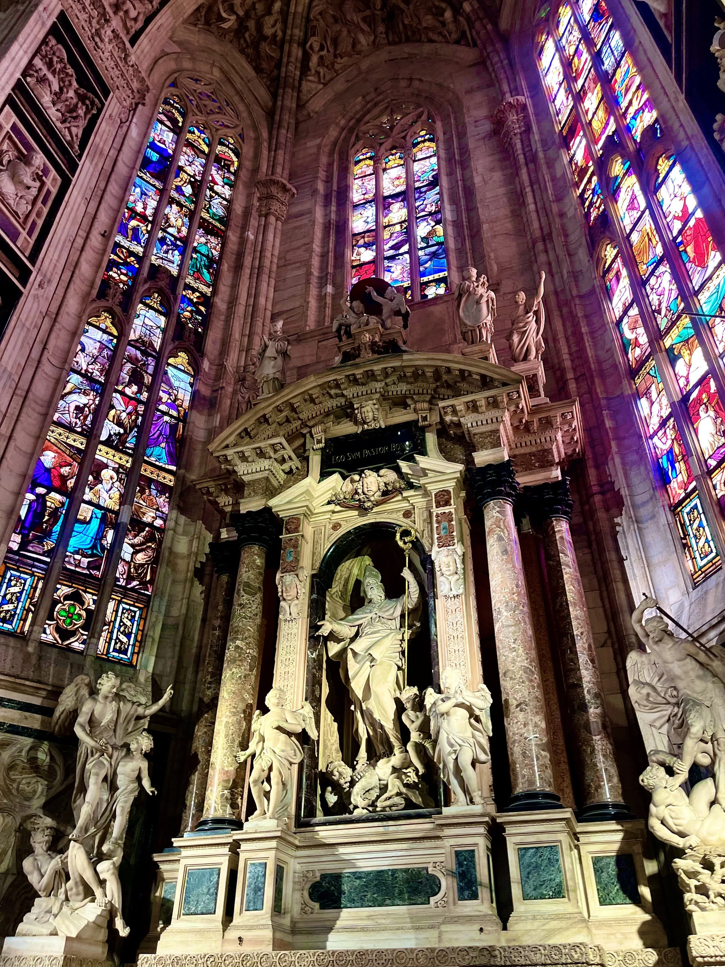 Interior architectural photograph of Milan Cathedral featuring stained glass windows and historic sculpture details.