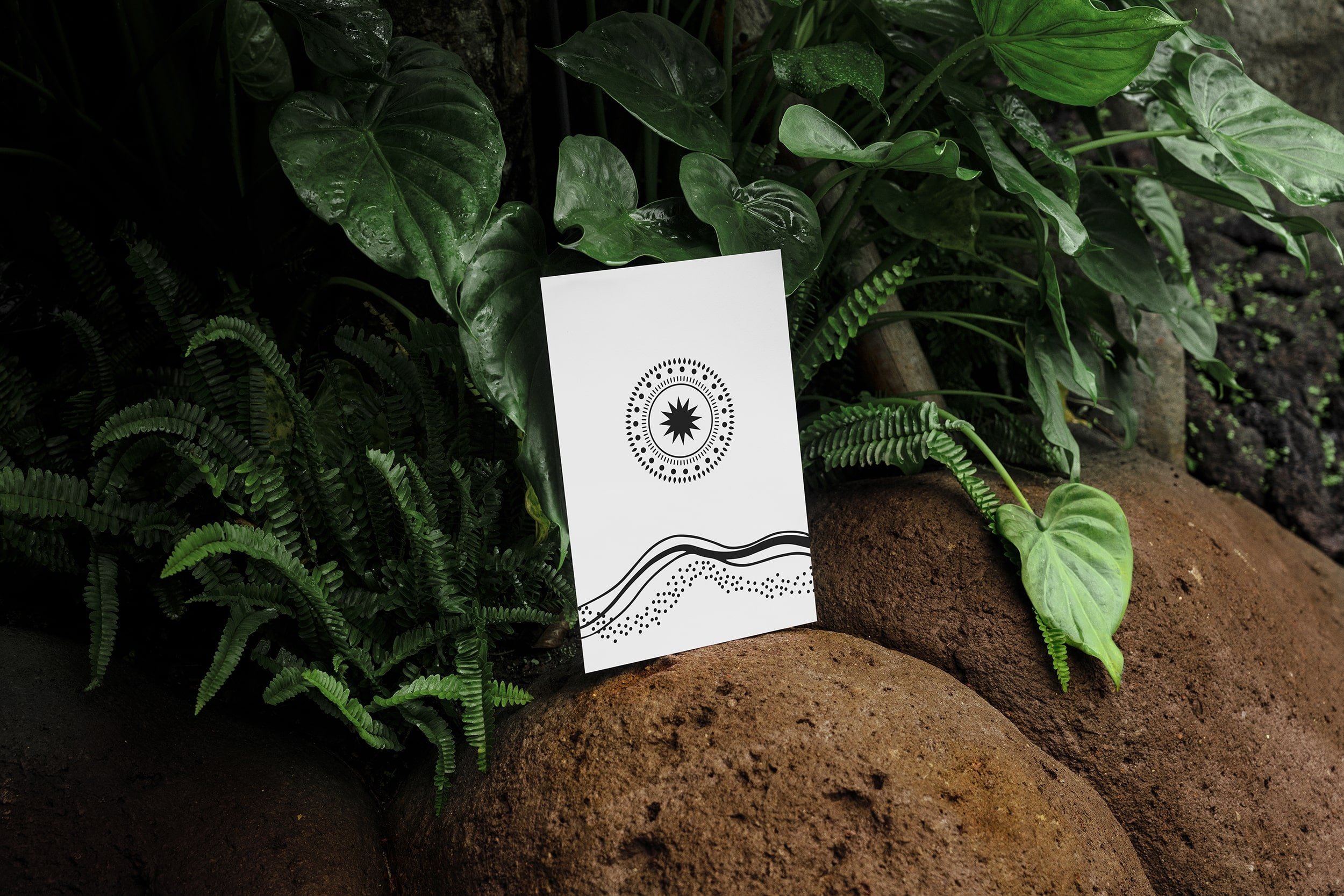 Black and white art print with abstract design and circular pattern, set against lush green foliage and rocks.