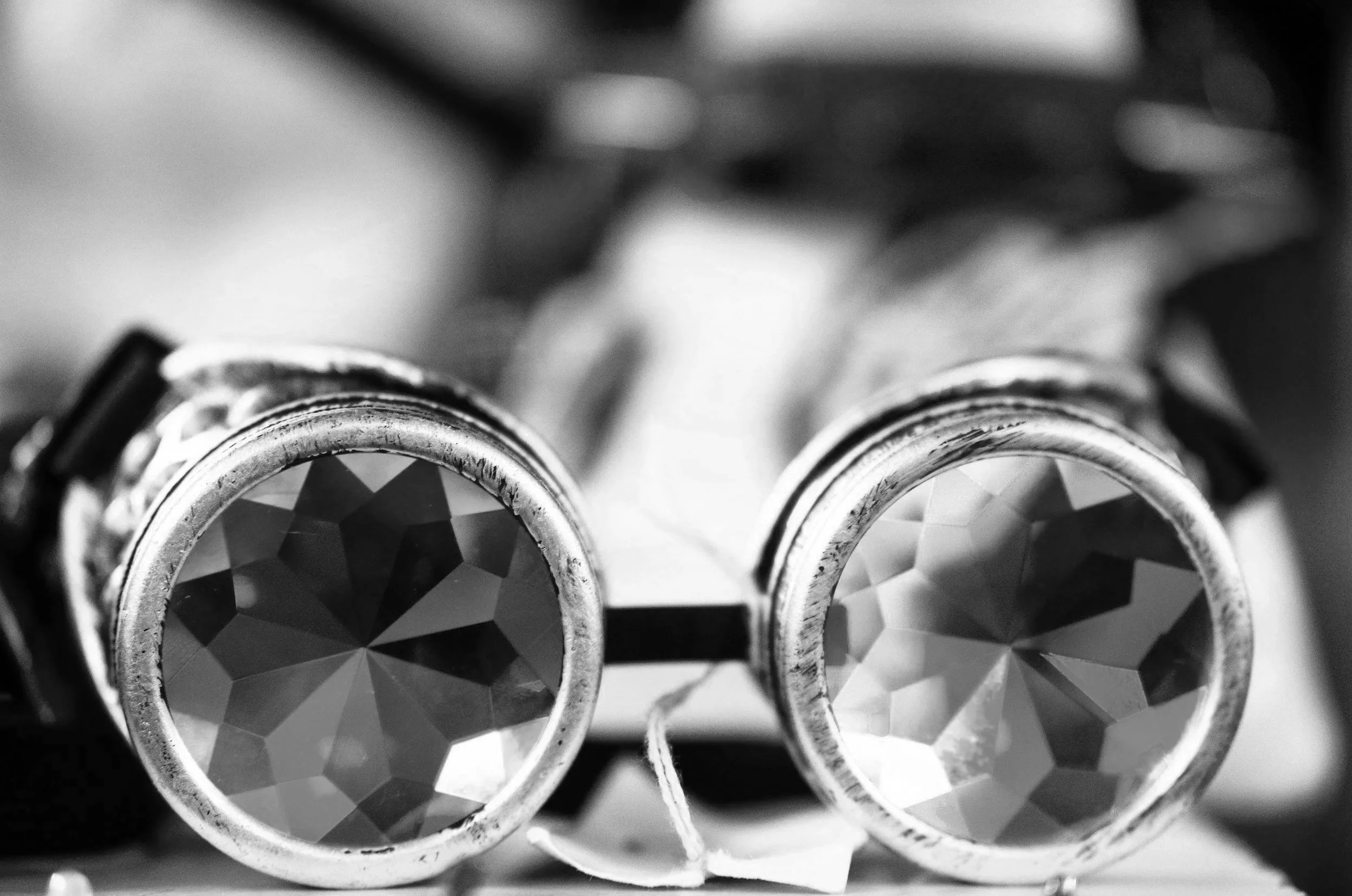 Close-up black and white photo of binoculars with large, faceted lenses in the foreground.