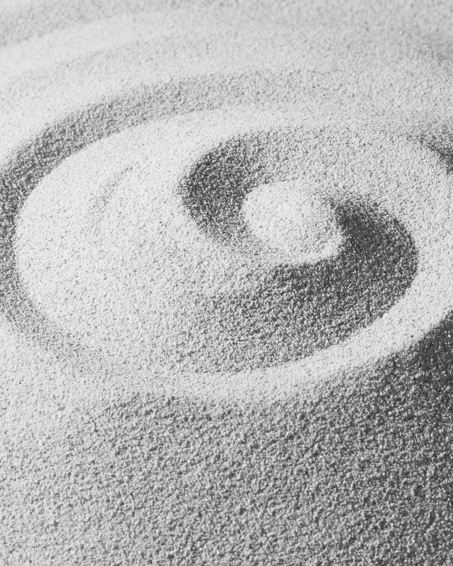 Close-up of sand with a spiral pattern drawn in it.