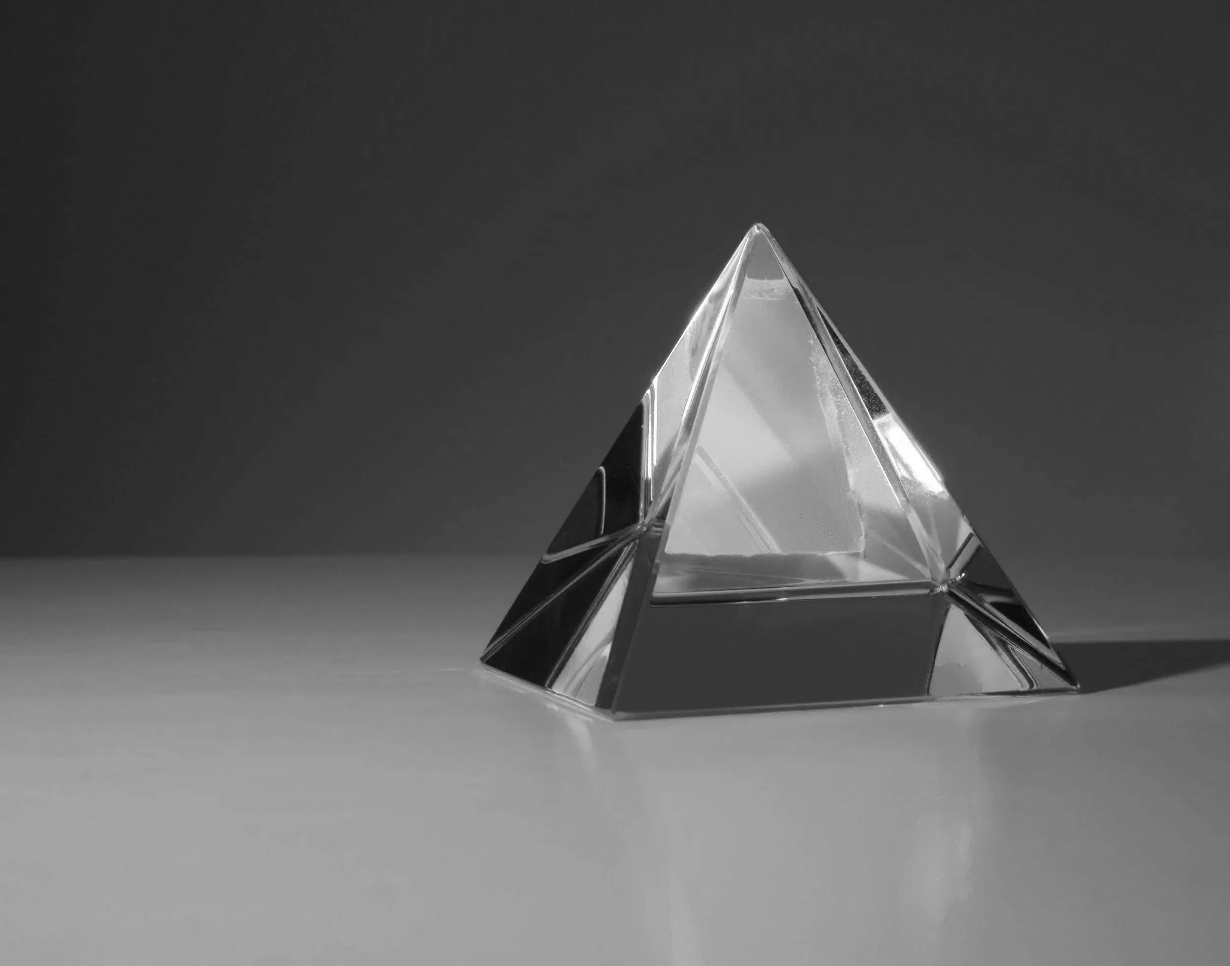 A transparent glass pyramid sculpture on a flat surface with a dark background.