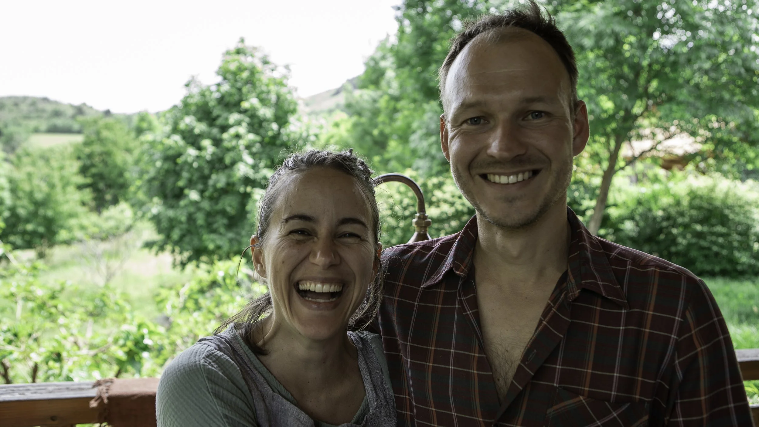 Jérôme et Emeline souriants devant un paysage verdoyant avec des arbres.