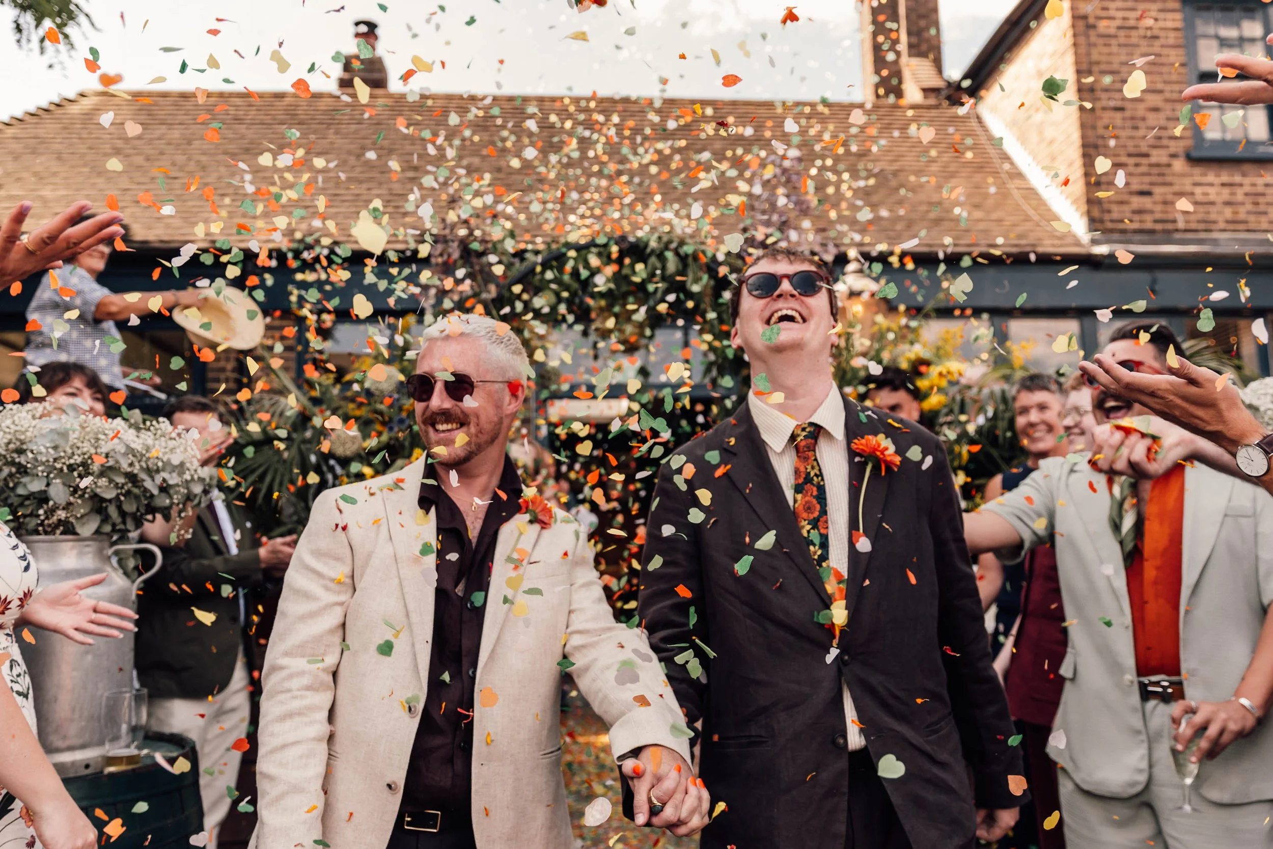 People holding hands and celebrating while colorful confetti falls during a wedding or festive event outdoors.