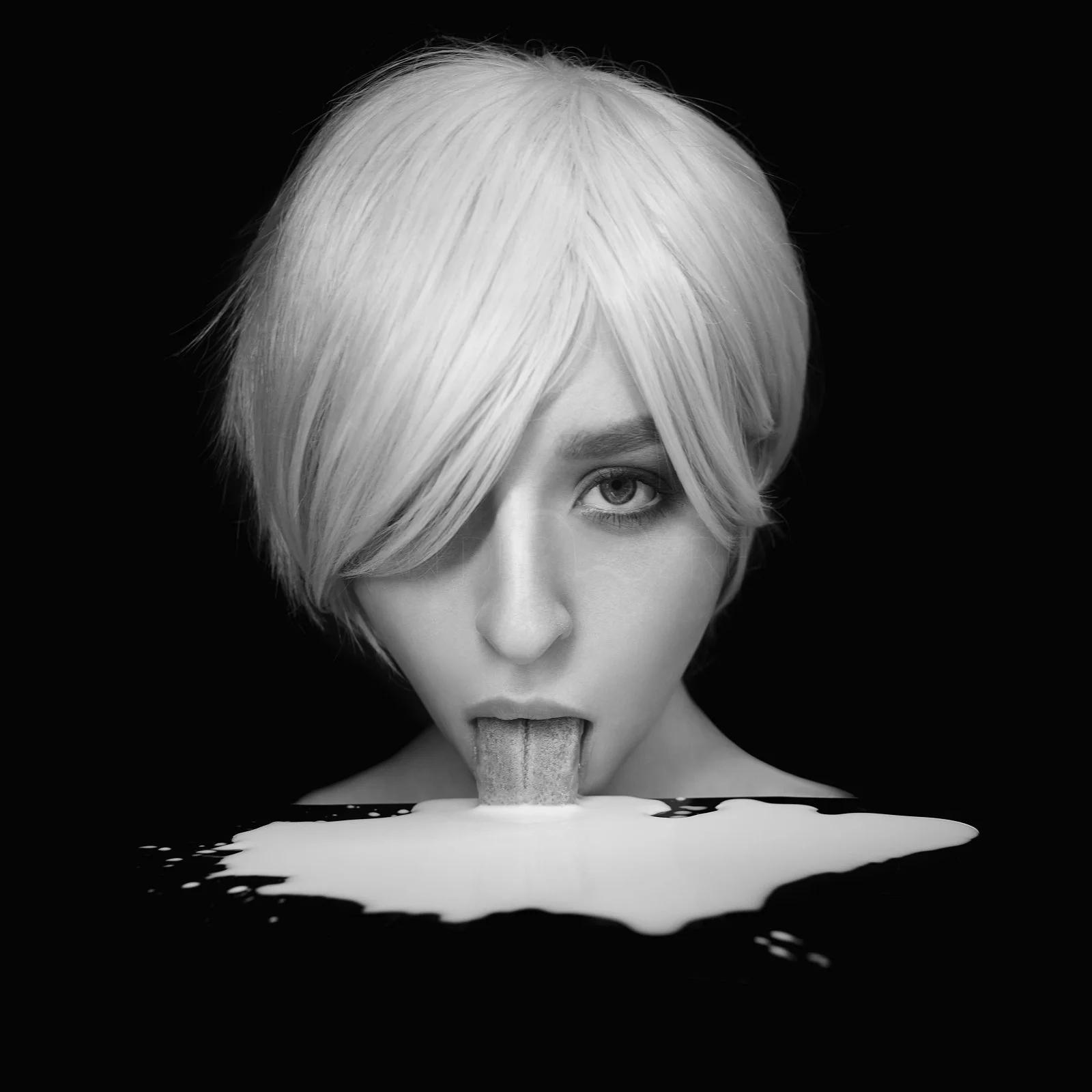 Black and white photo of a woman with light-colored, short, layered hair, licking a spoon dipped in a bowl of milk or cream.