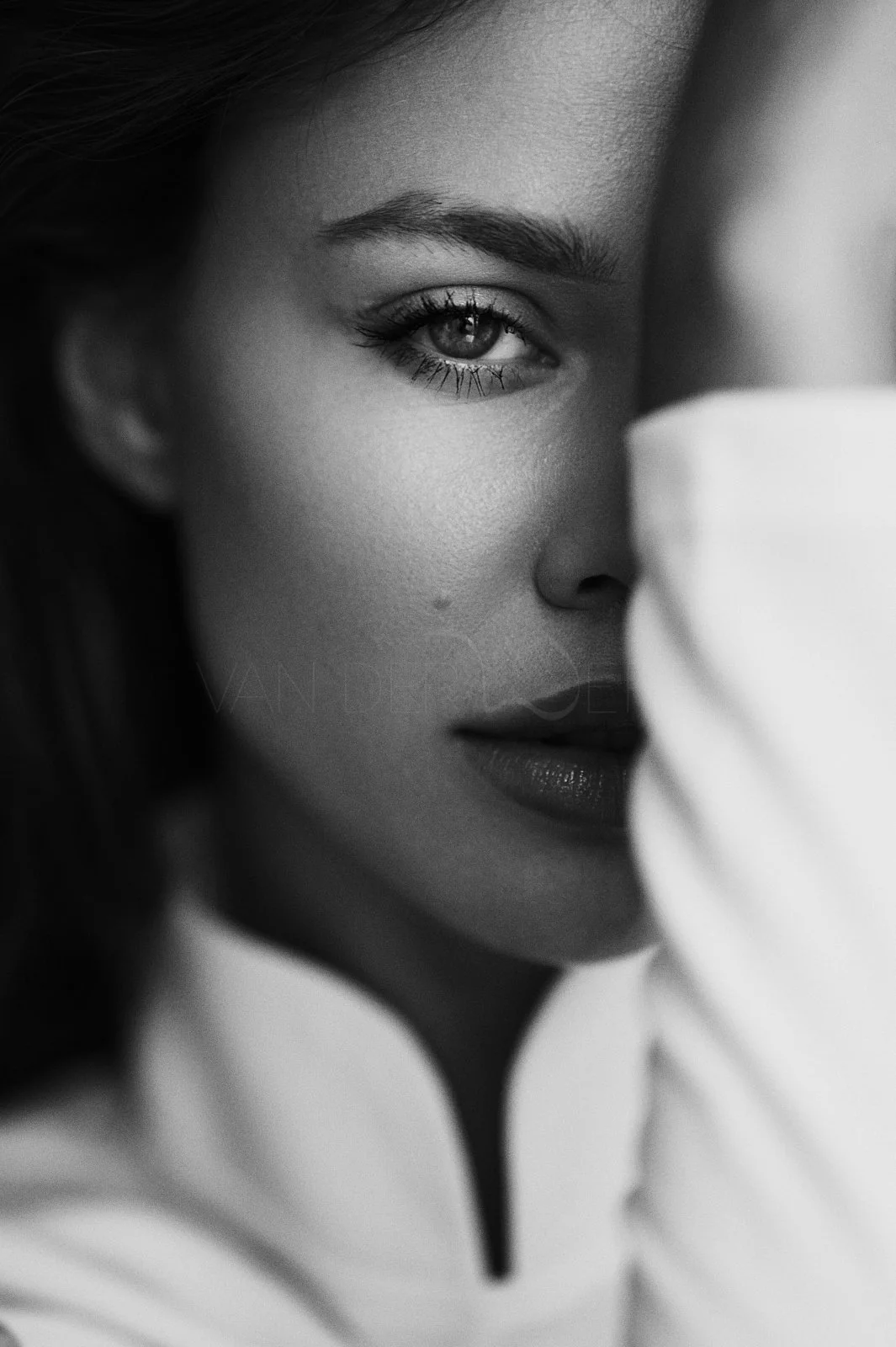 Close-up of a woman with one eye visible, makeup, and dark lipstick, partially obscured by a white fabric.