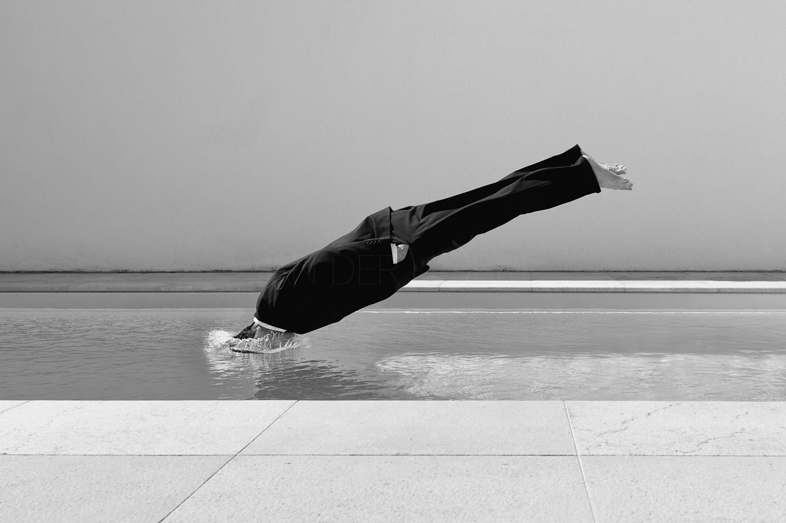 A person in a business suit performing a handstand on the edge of a swimming pool.