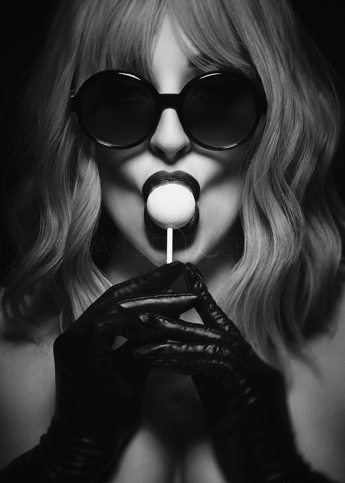 A black and white photo of a woman wearing round sunglasses and black gloves, holding a lollipop near her lips.