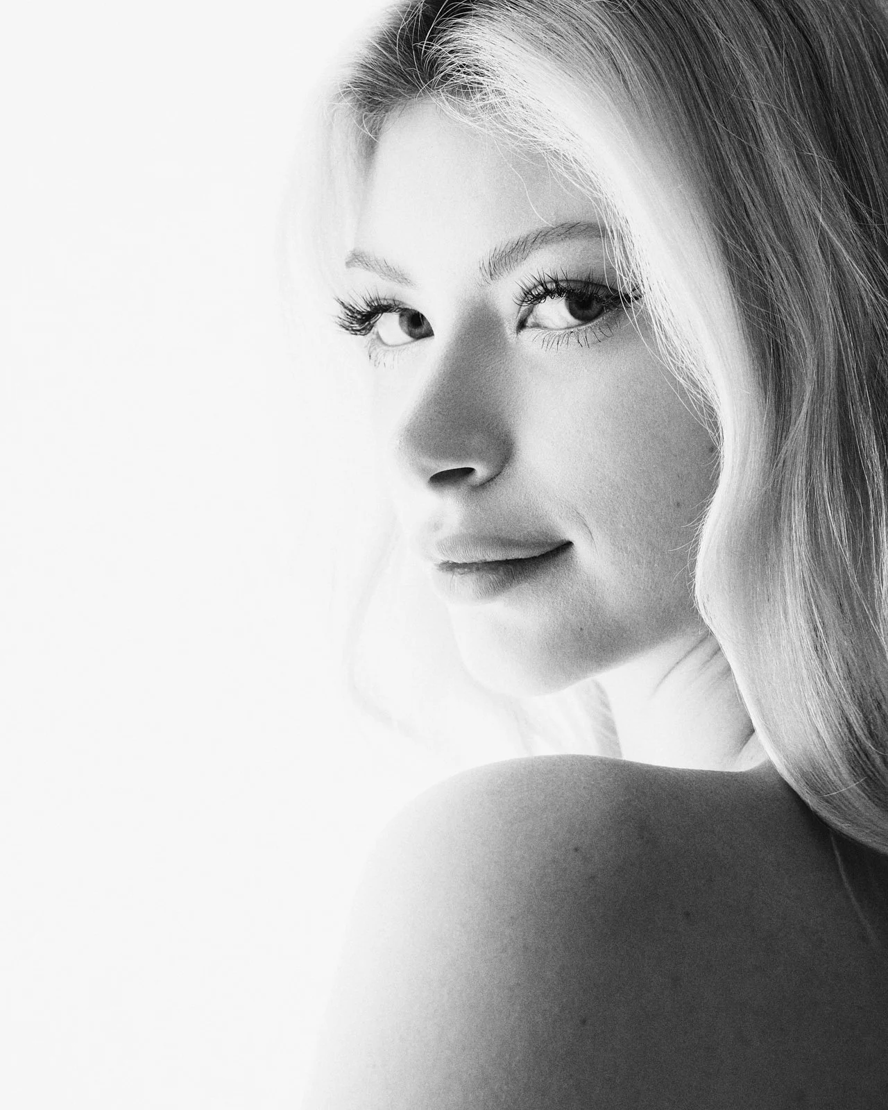 Black and white close-up portrait of a woman with long hair, looking over her shoulder with a slight smile.