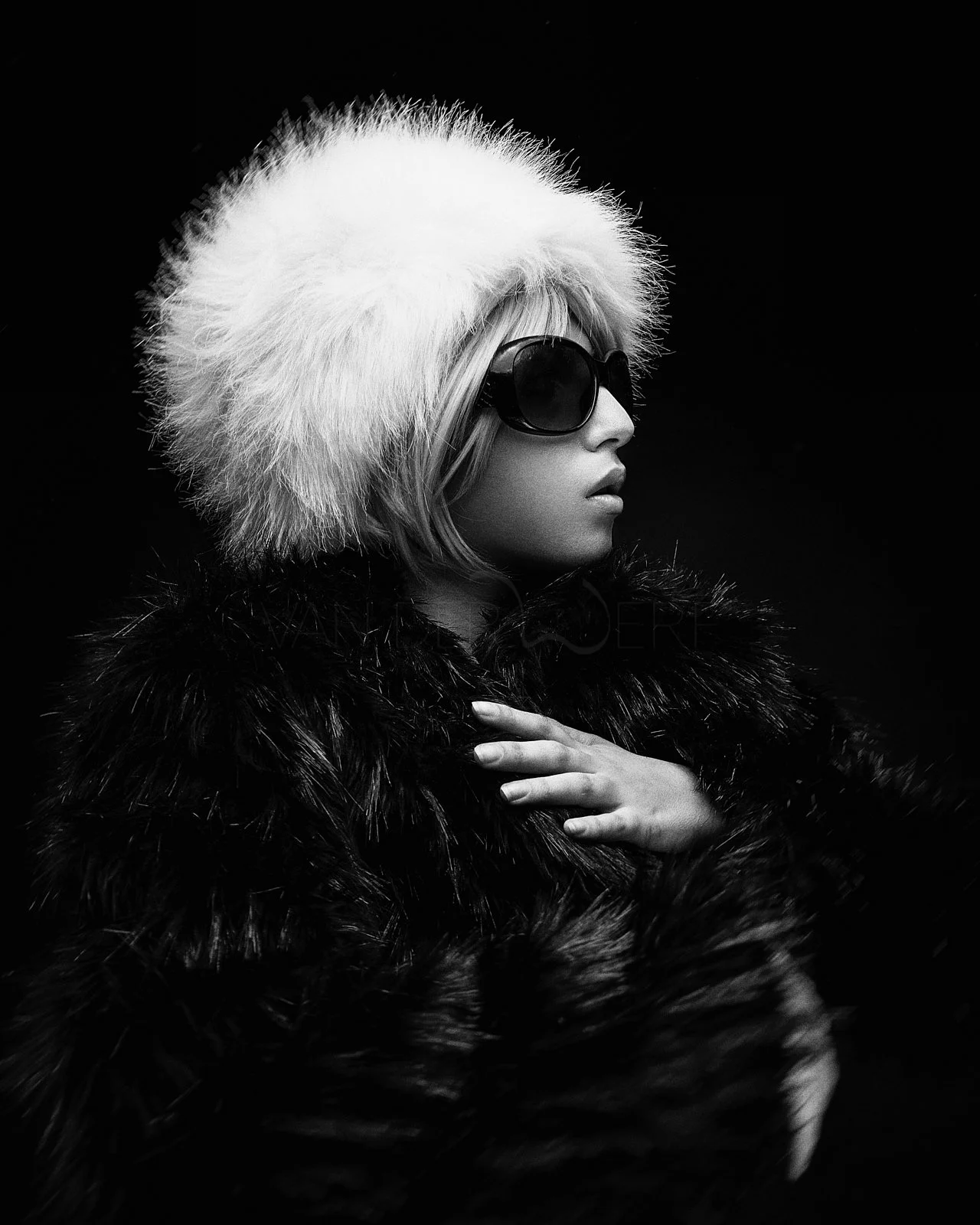 Black and white photo of a woman wearing a fur hat, large sunglasses, and a fur coat, with her hand on her chest.