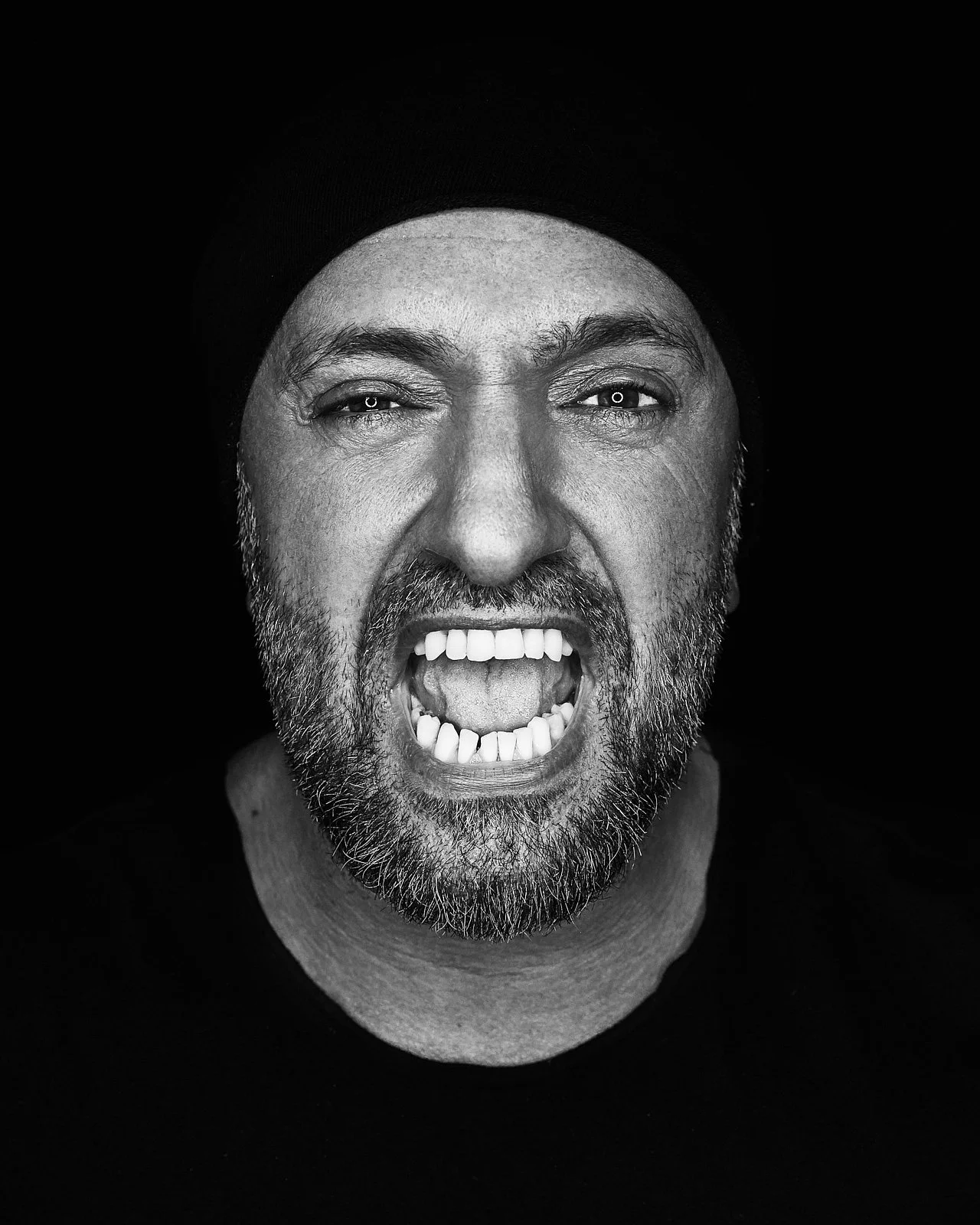Close-up black and white photo of a middle-aged man with a beard, expressing anger or shouting.