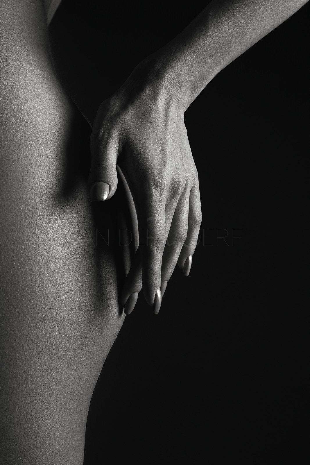 Close-up black and white photo of a person's hand resting on their thigh against a dark background.