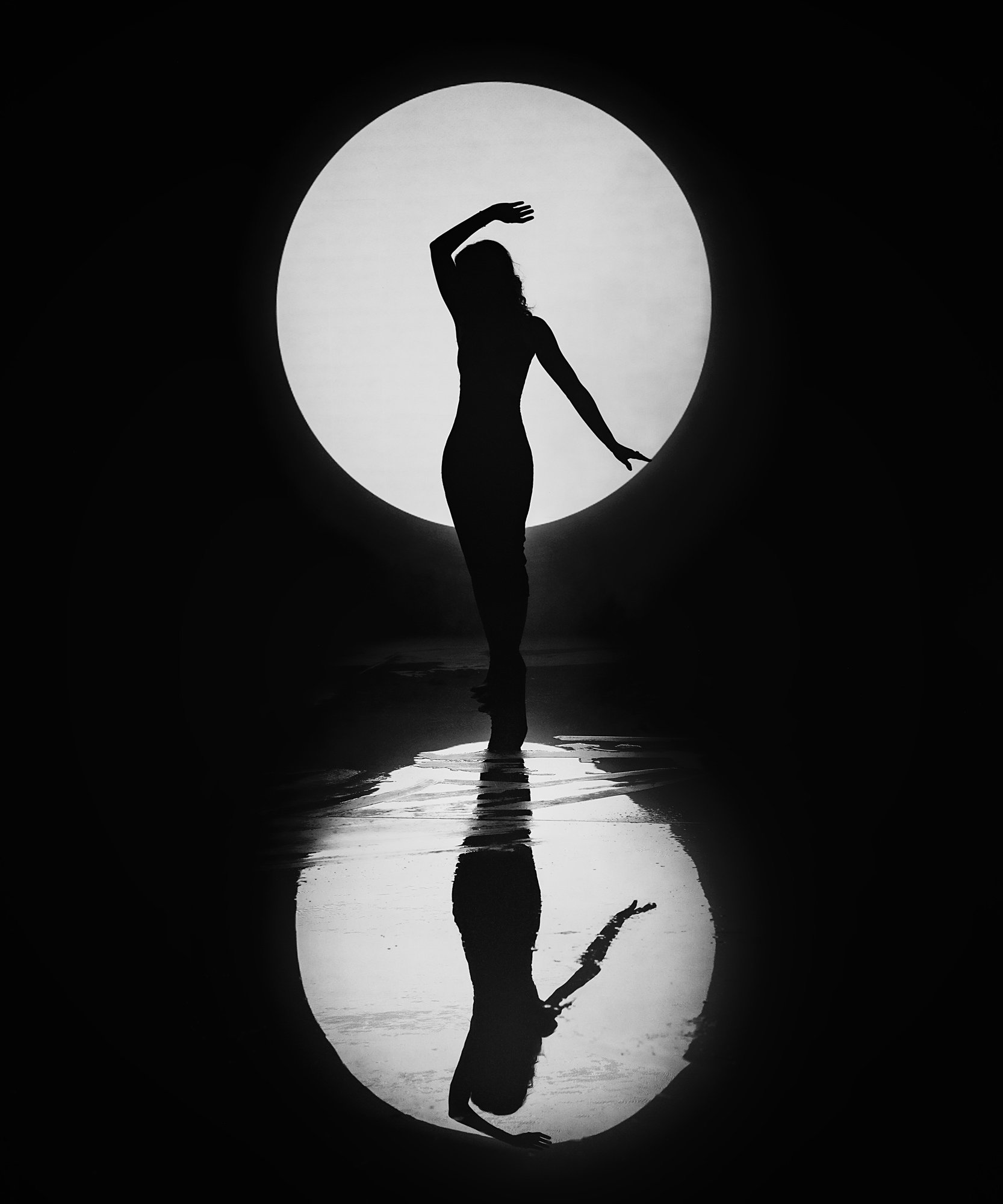 Silhouette of a woman standing in a circular opening with a bright moon behind her, with her reflection seen in water below.