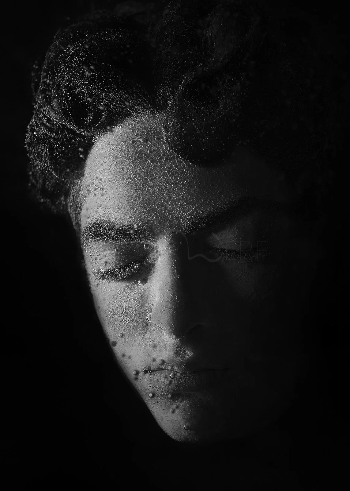 Close-up black and white photo of a woman's face with her eyes closed, behind a glass surface covered in condensation and water droplets.