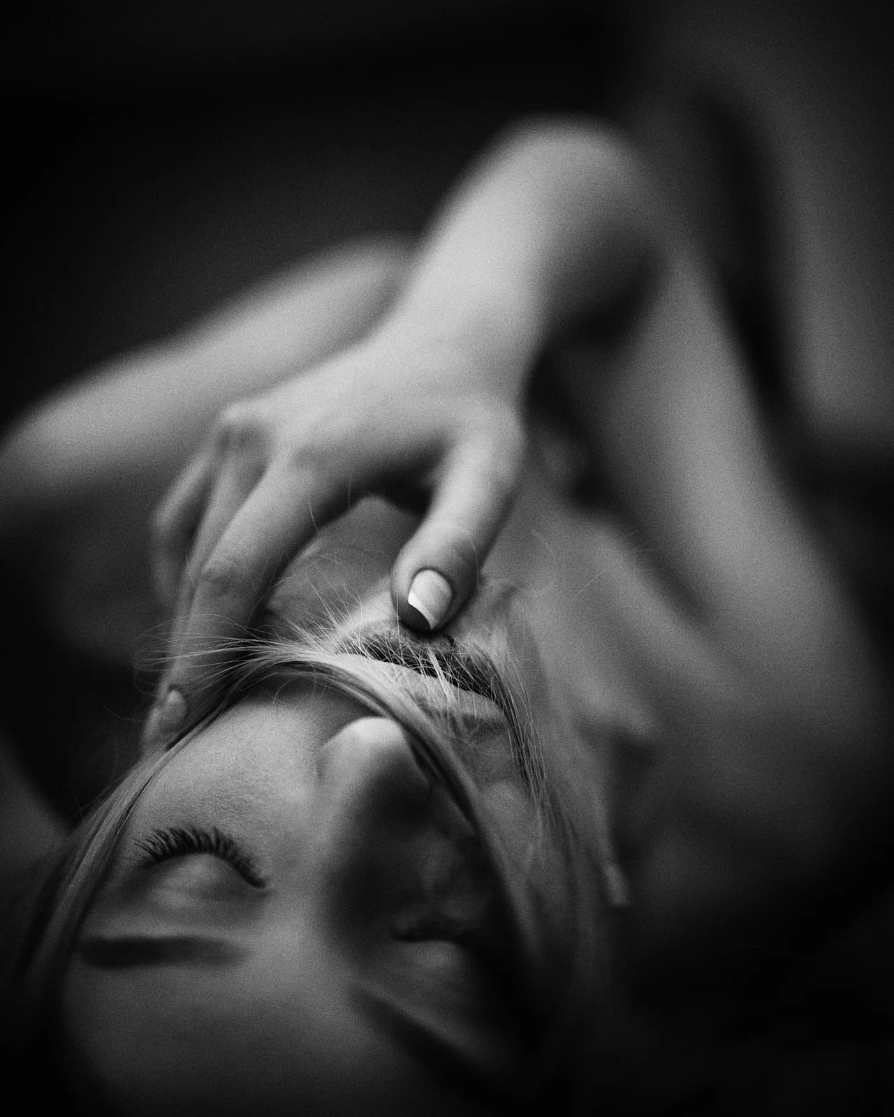 Black and white close-up photo of a woman's face with her eyes closed, her fingers gently touching her forehead.