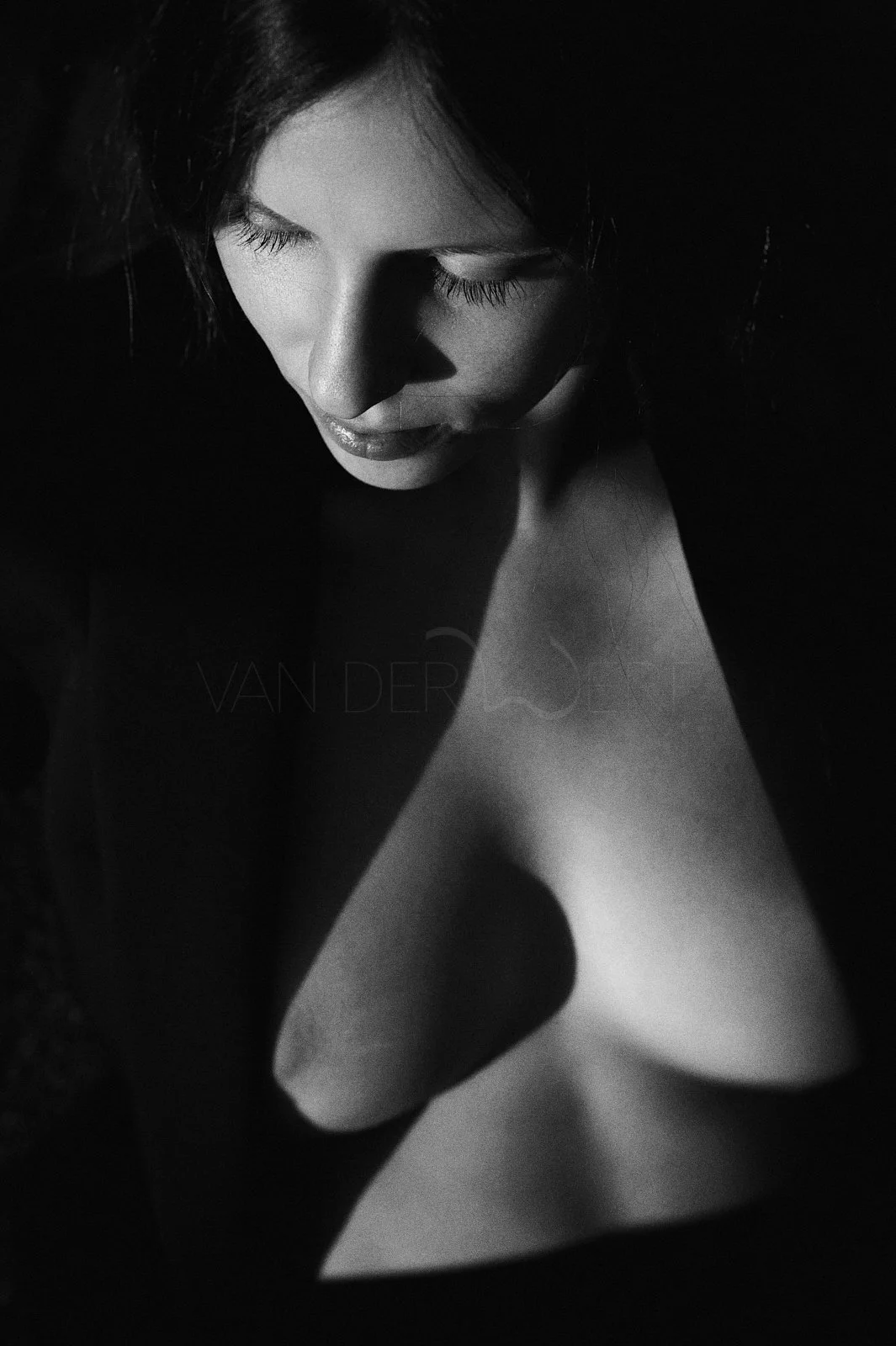 A black and white photograph of a woman with closed eyes, soft lighting highlighting her face and a heart-shaped object in the foreground.