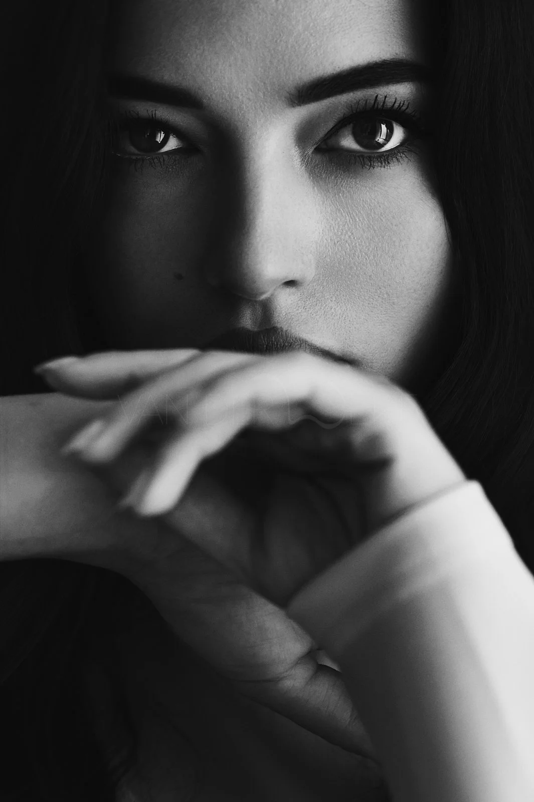 Close-up of a woman with dark hair, resting her chin on her hand, black and white photograph.
