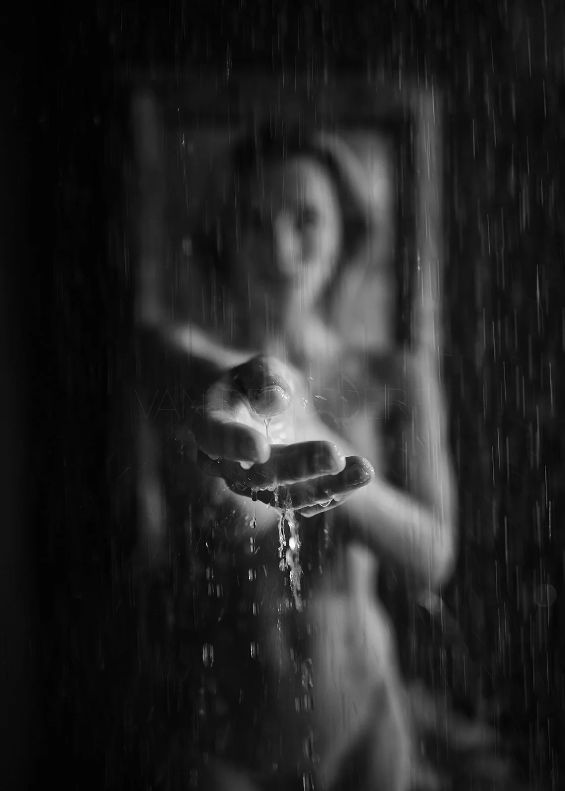 A black and white photo of a person behind a rain-covered glass, with water dripping from their hand extended towards the camera, creating a moody and artistic effect.