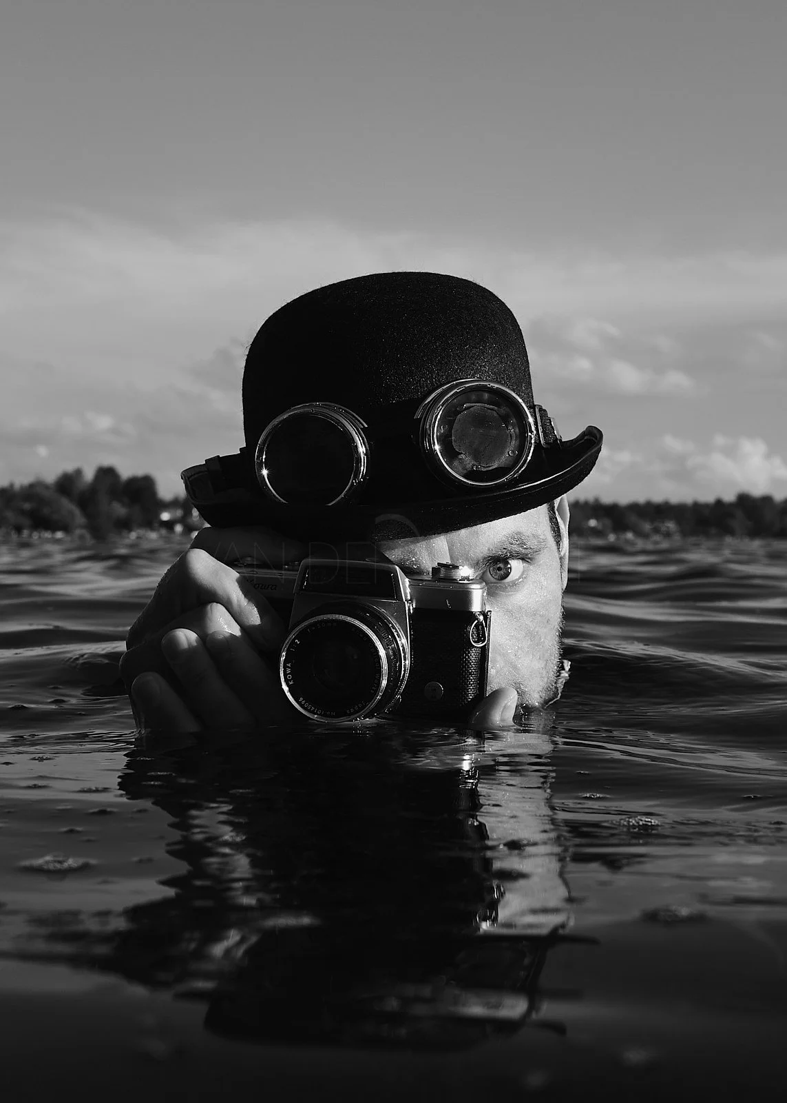 A person wearing goggles and a bowler hat, holding a vintage camera, partially submerged in water, with a landscape and cloudy sky in the background.