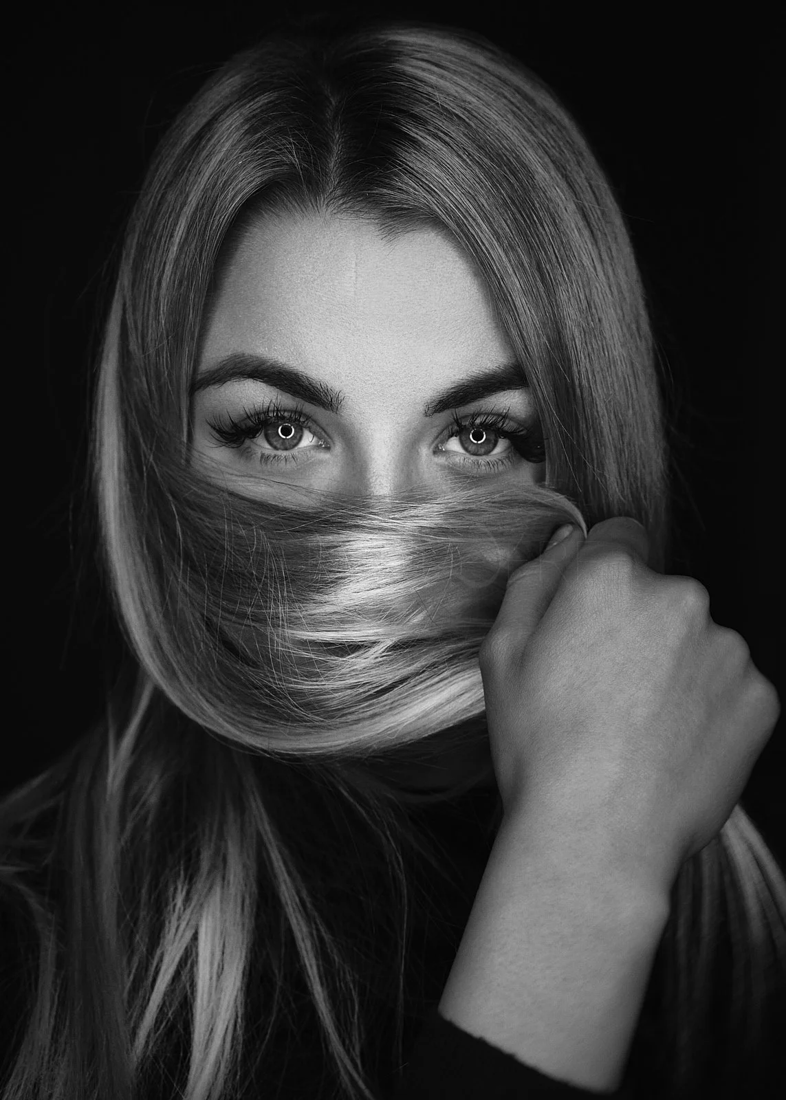 Black and white portrait of a woman with long hair covering part of her face, looking directly at the camera with intense eyes.
