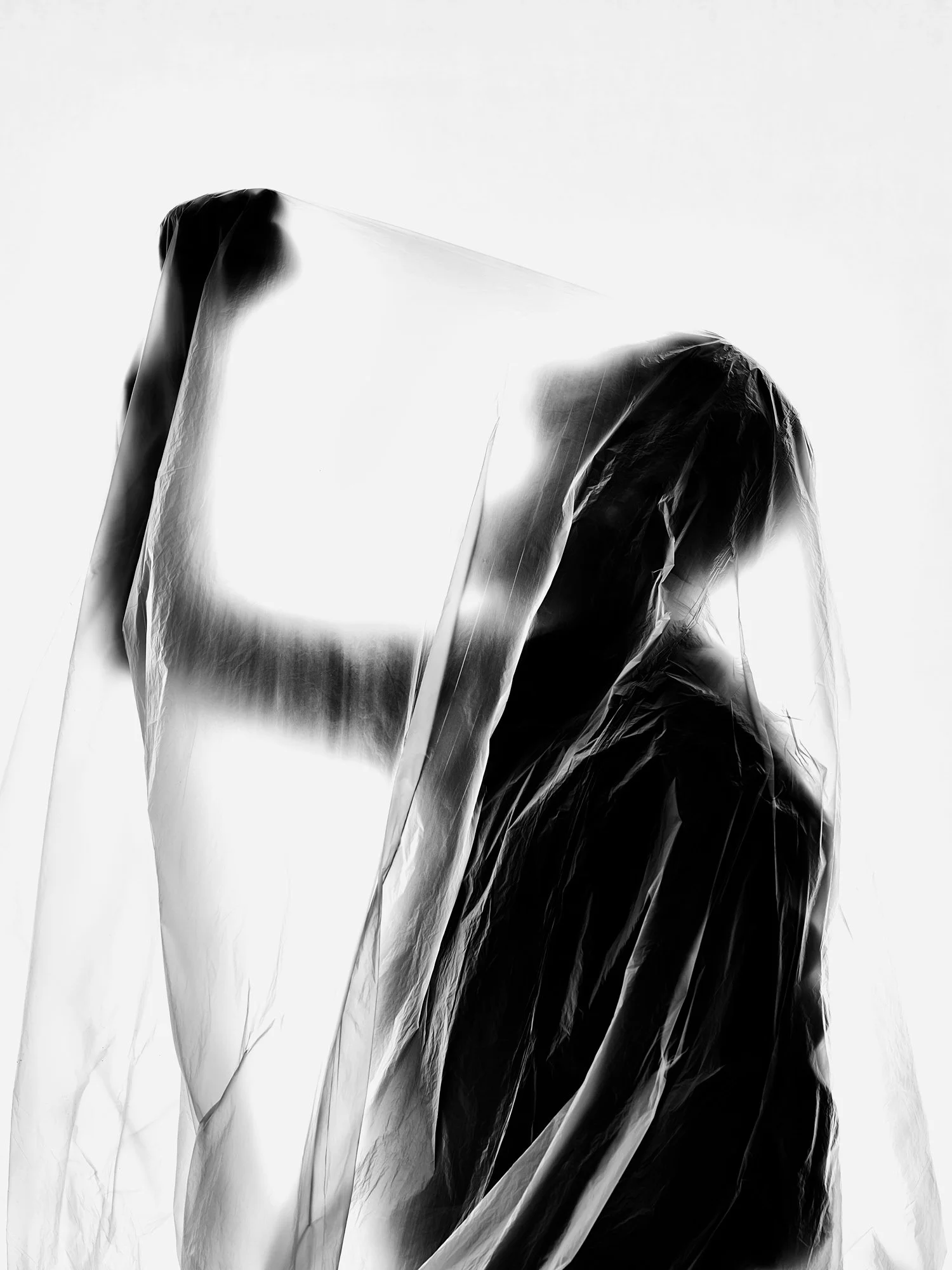 Black and white abstract photograph of a person wrapped in plastic, with a glow behind the head and shoulders, creating a surreal and artistic effect.