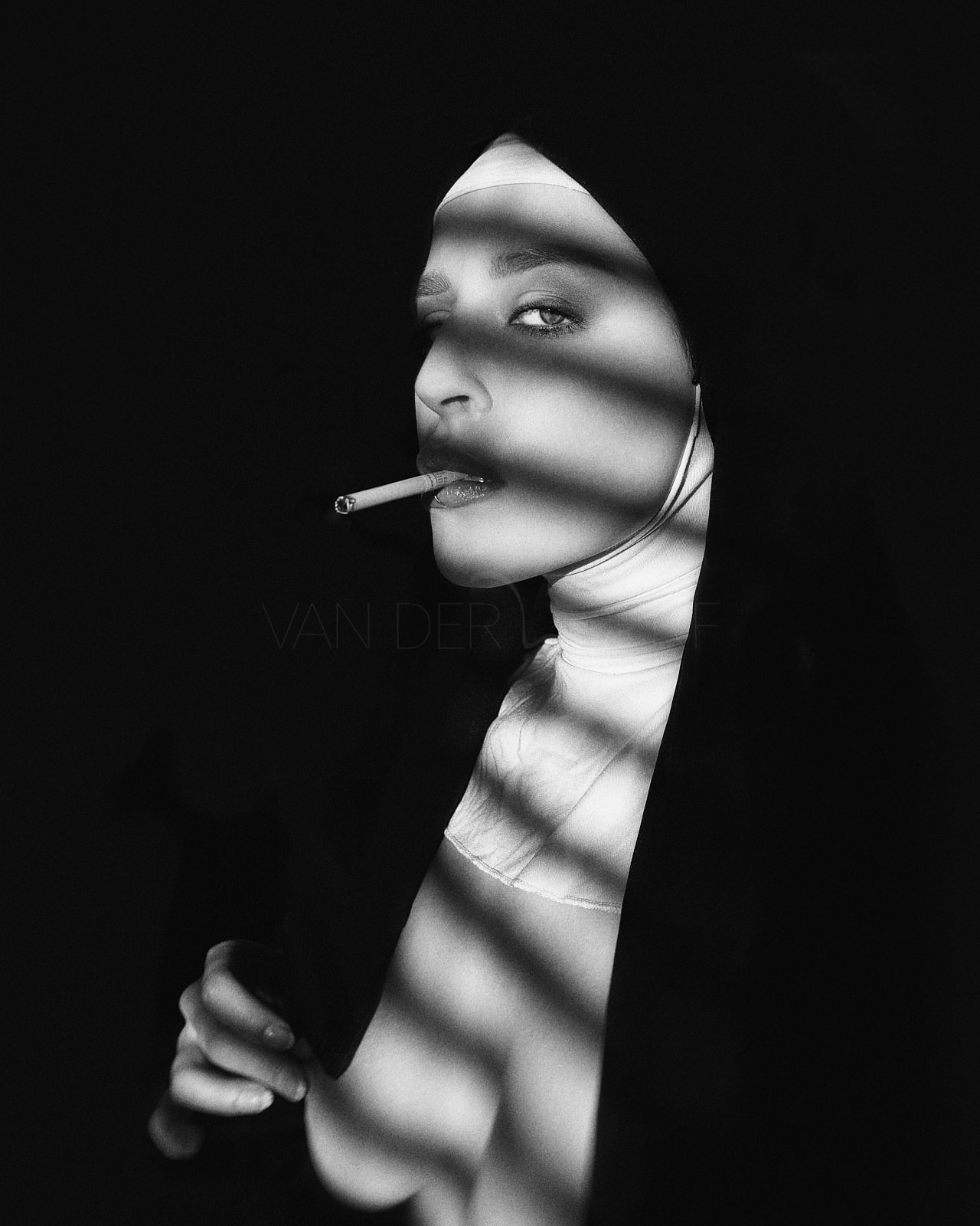 Black and white portrait of a woman with a cigarette in her mouth, wearing a hooded outfit, with striped shadows across her face and body.