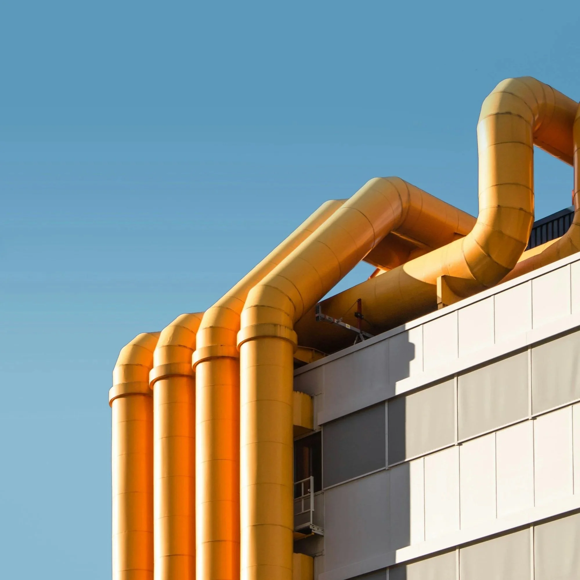 Yellow industrial pipes on the side of a modern building under a clear blue sky.