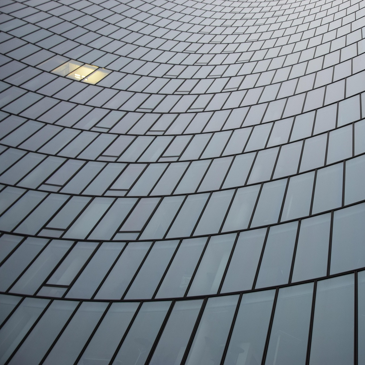 Close-up of a modern glass building with a curved facade made of reflective windows aligned in horizontal rows.