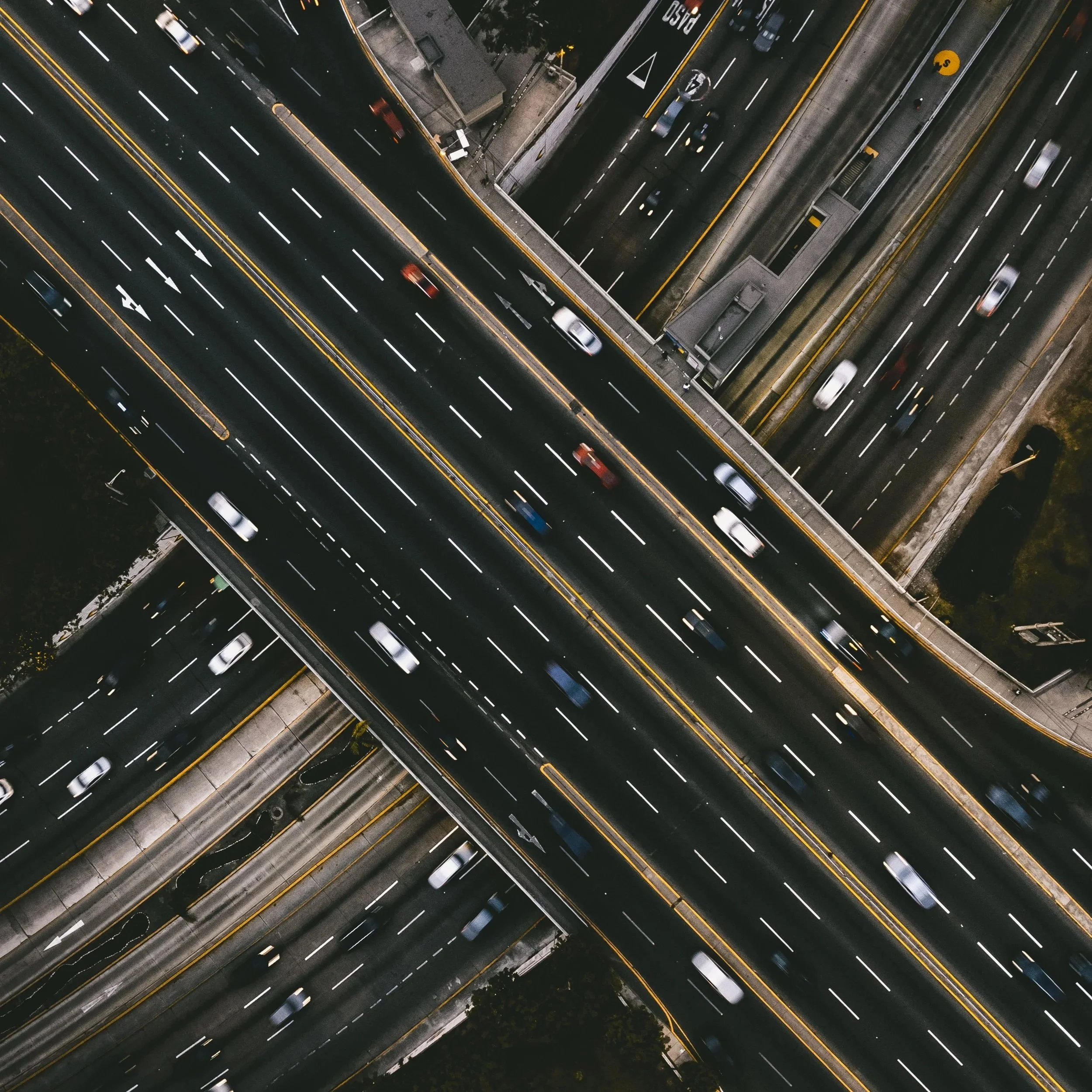 Aerial view of a multi-level highway at night with cars moving, illuminated by streetlights and road markings.
