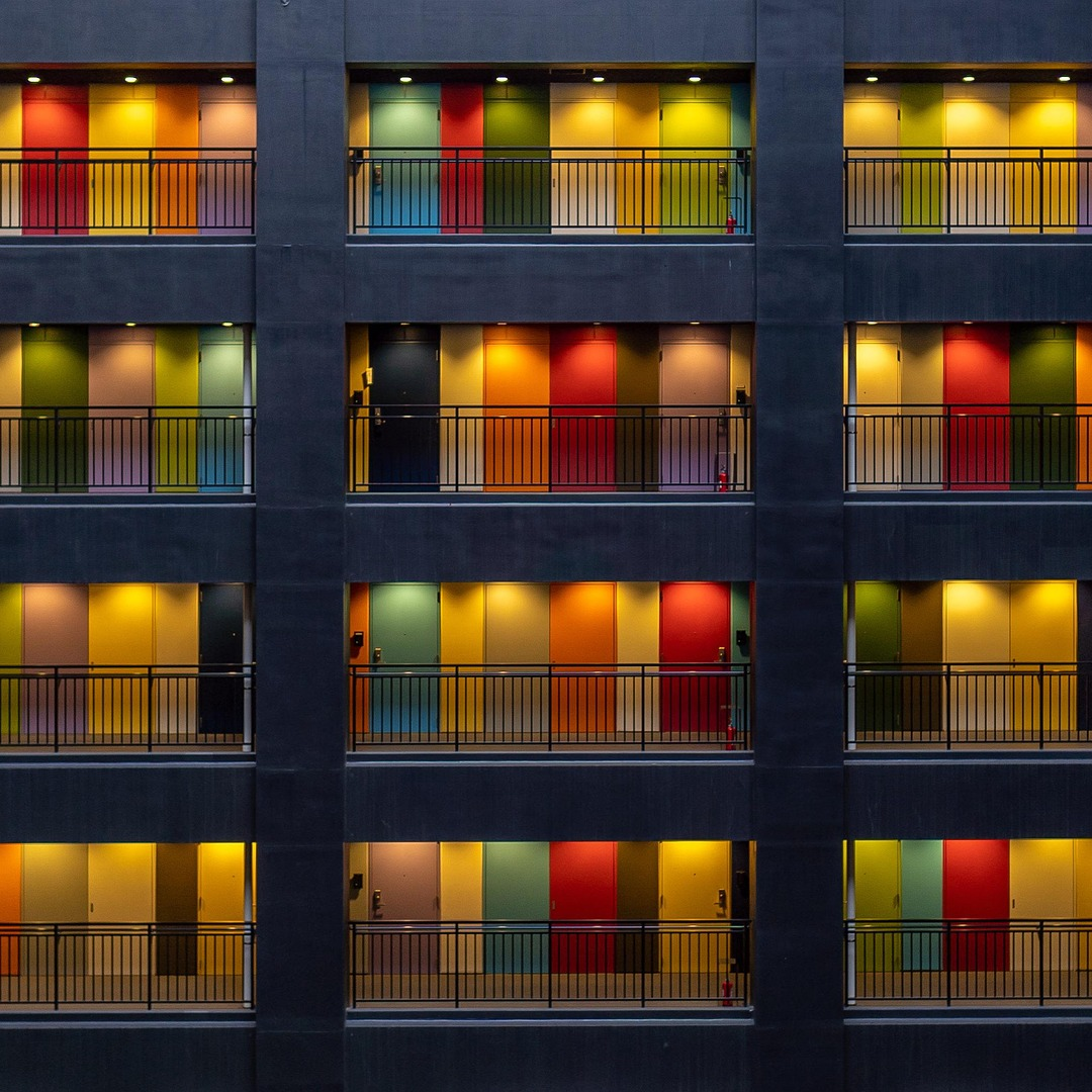 Multiple apartment balconies with colorful illuminated doors in a dark building