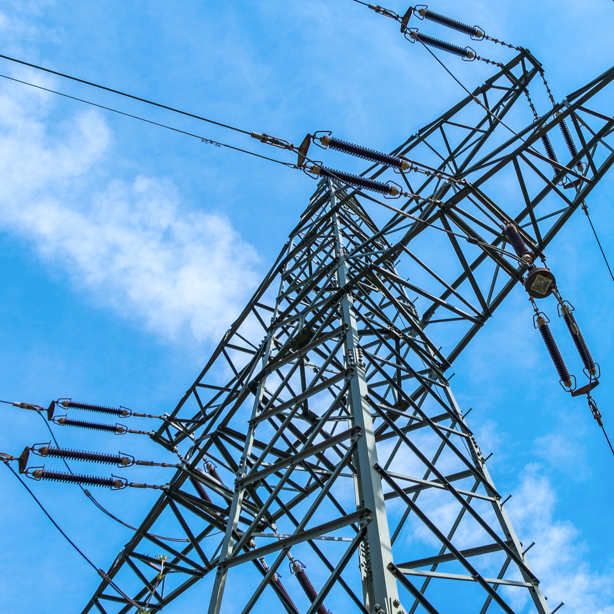 A tall electrical transmission tower with wires and insulators against a blue sky with some clouds.