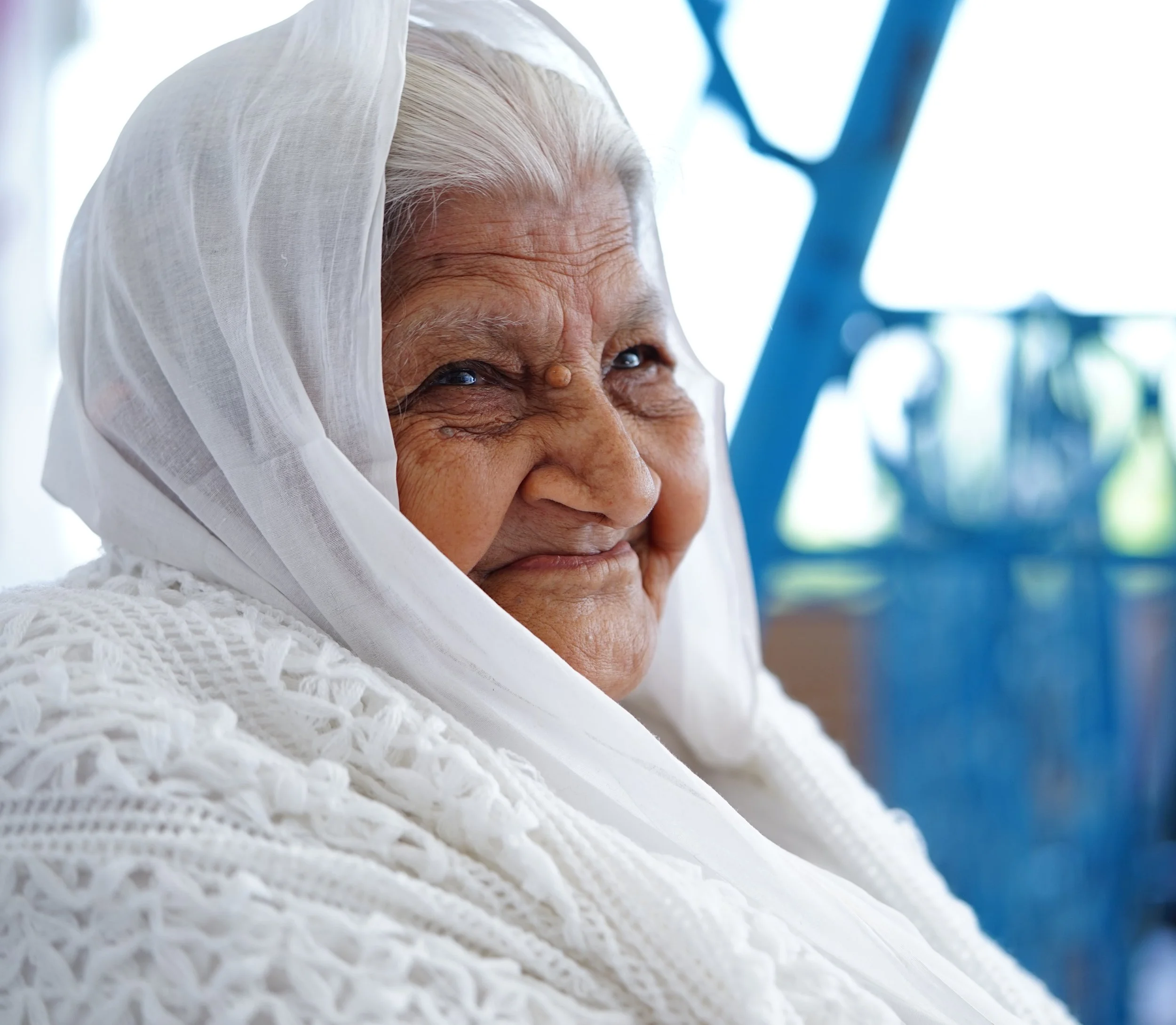 An older woman of South Asian heritage, wearing white and smiling.