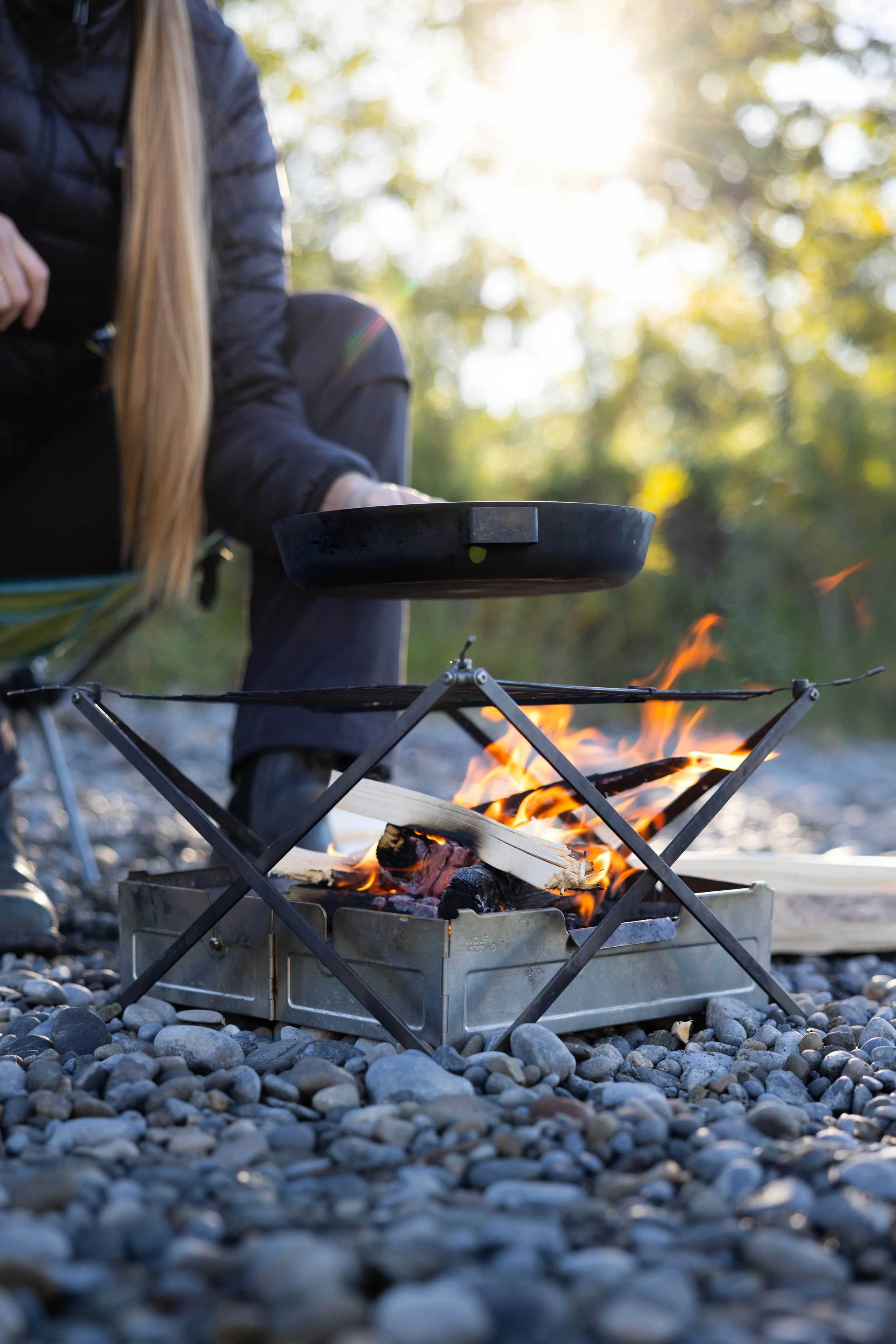 person holding cast iron pan over small campfire
