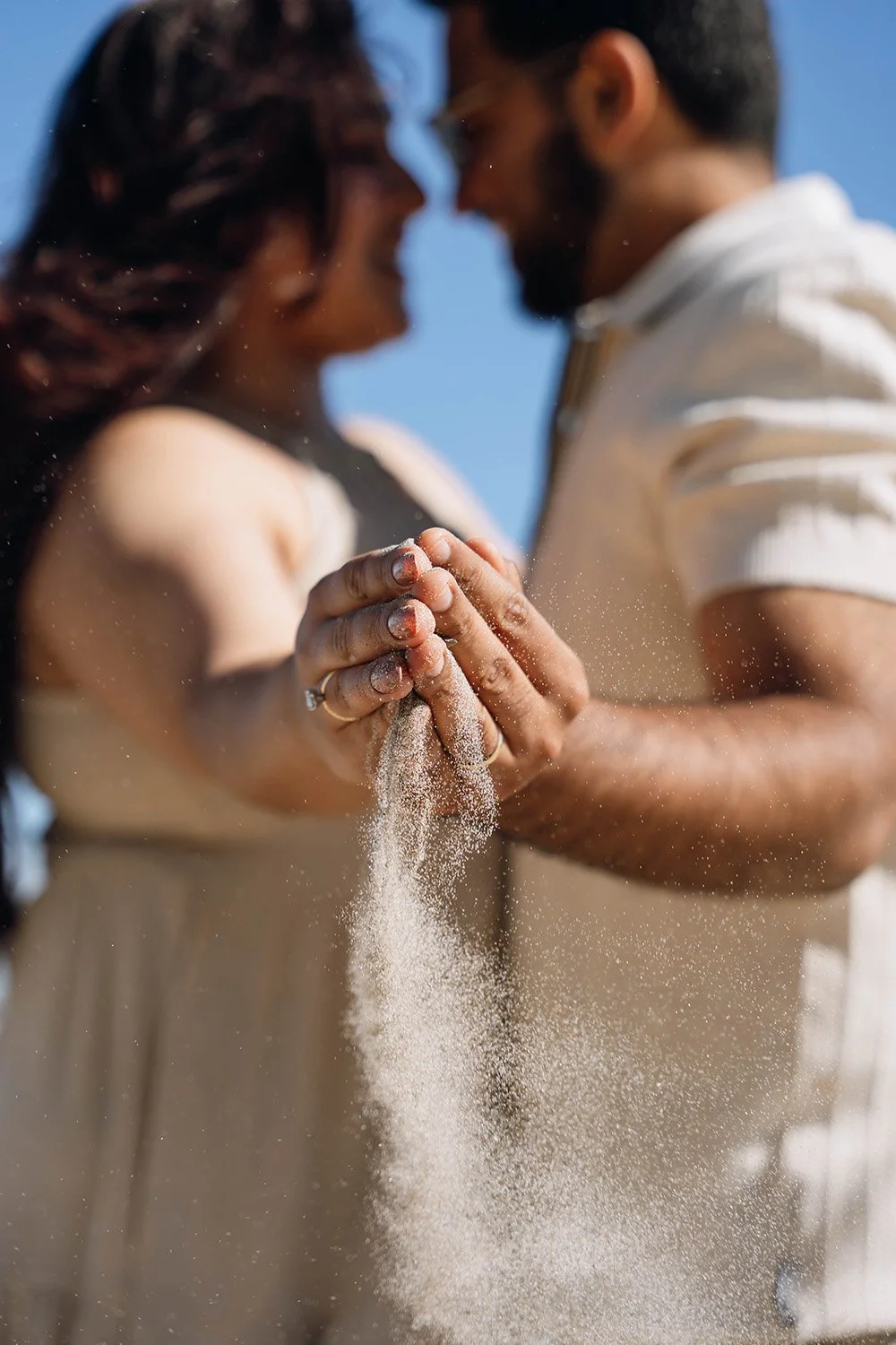 Engaged couple letting sand slip through their hands while showcasing their wedding rings during an Ontario engagement session