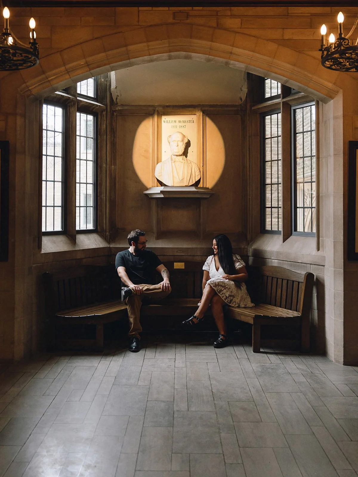 An engaged couple sits together on a bench on a university campus in Hamilton, Ontario