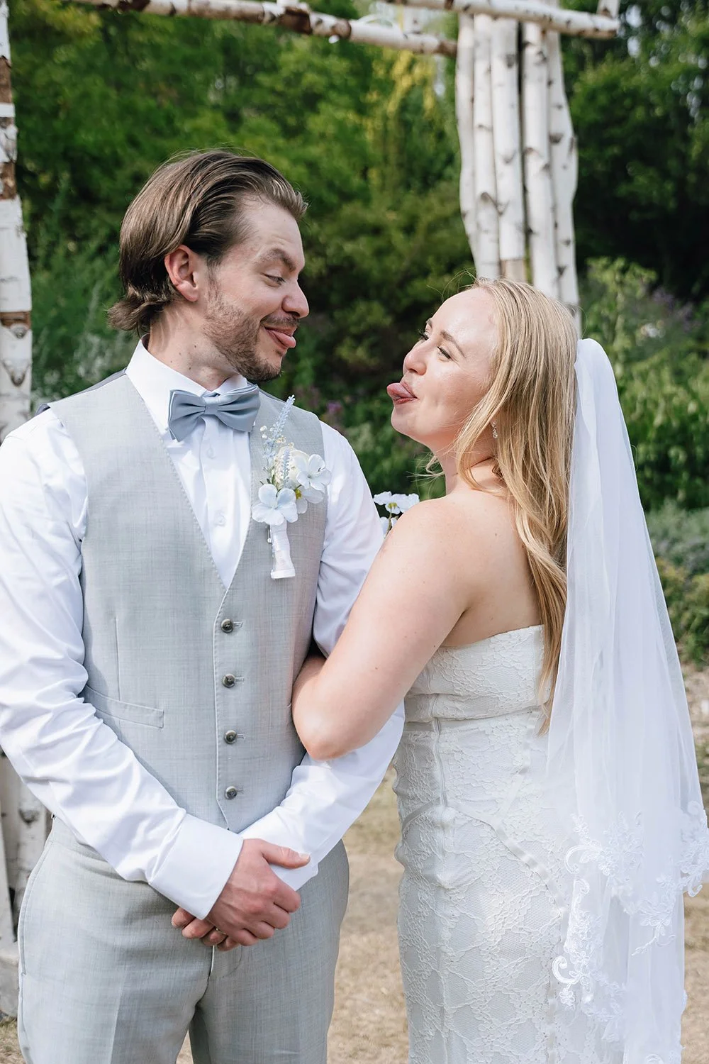 Bride and groom playfully sticking out their tongues during fun wedding portraits in Ontario