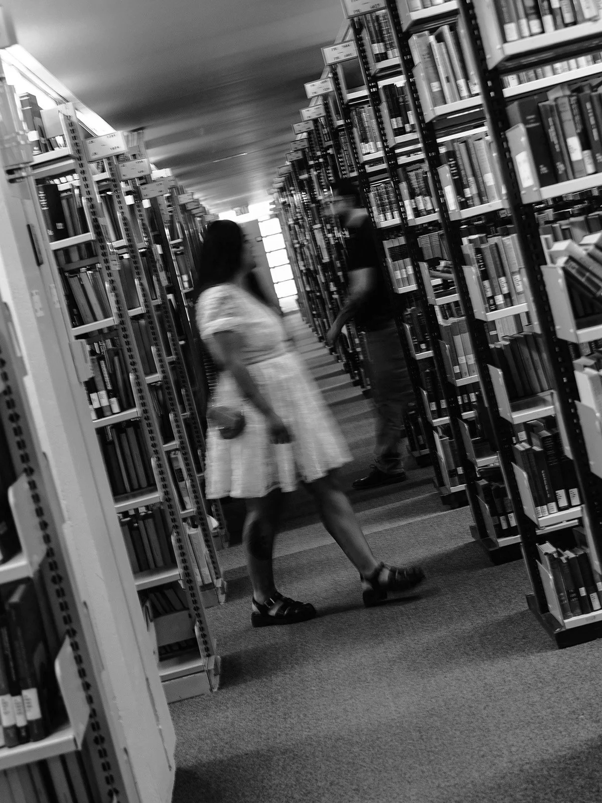 Cinematic, blurry moment as an engaged couple walks past each other in a university library.