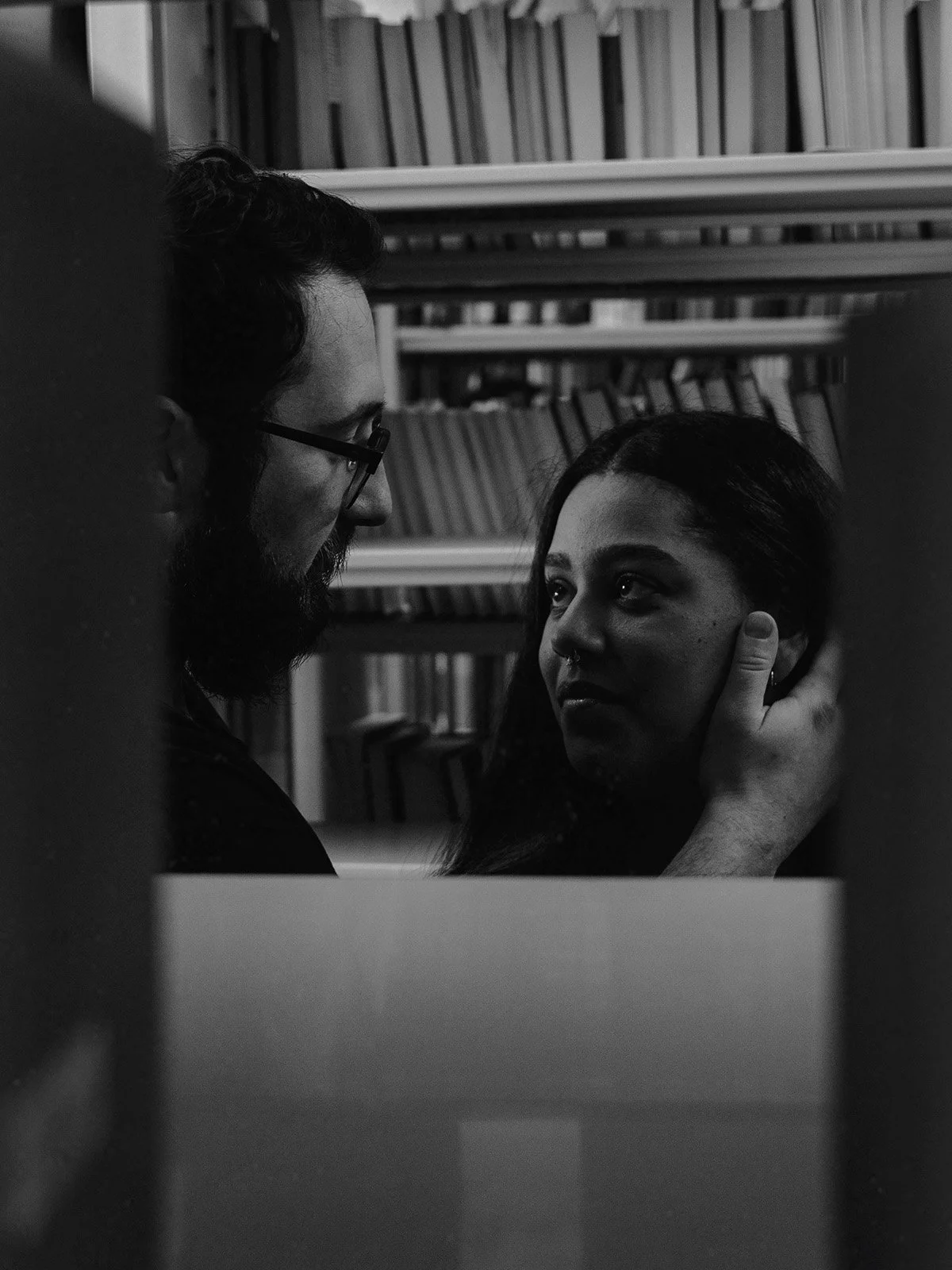 A man embraces his partner in the middle of library shelves.