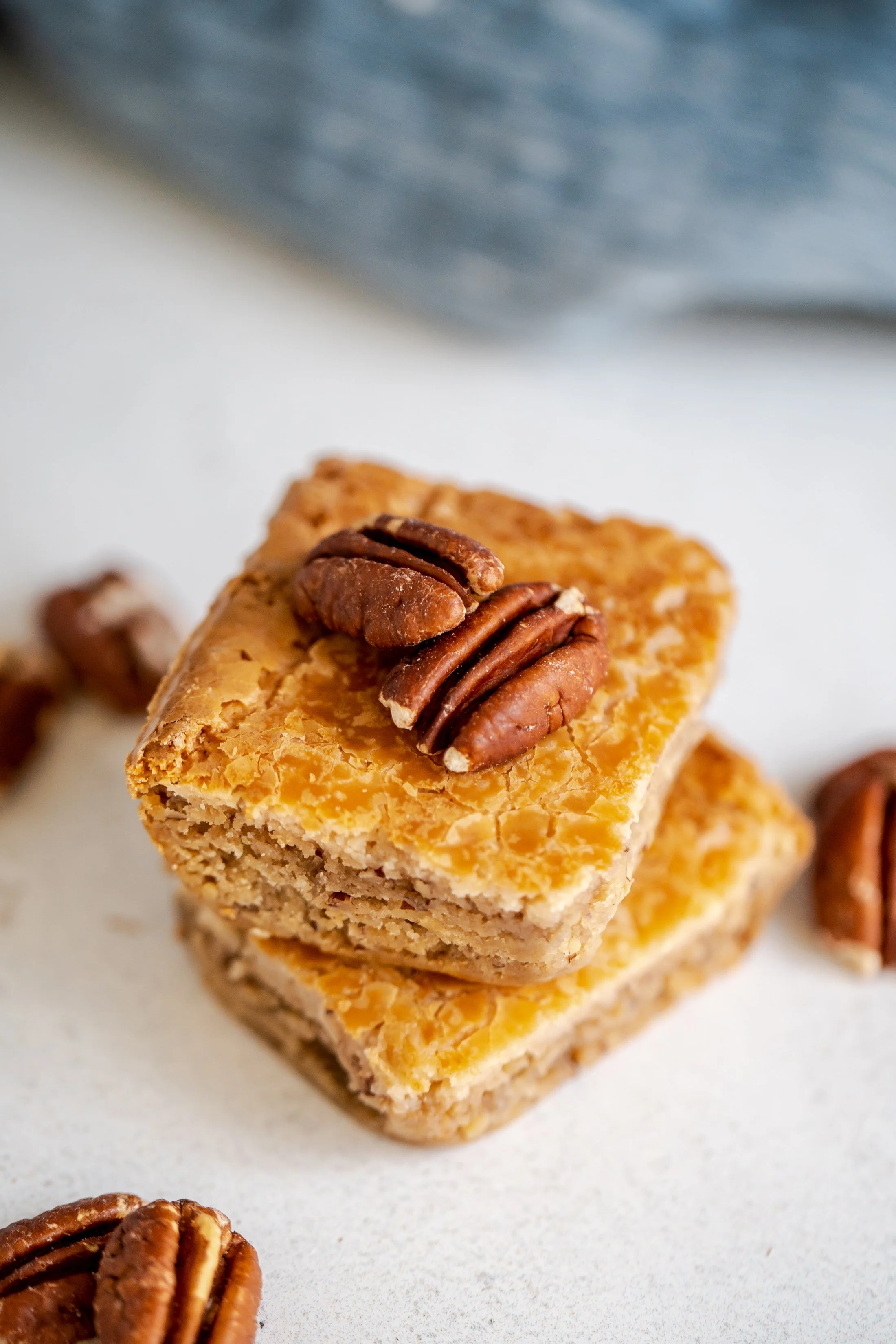Close-up of a stack of homemade granola bars topped with pecans, with a few pecans and chocolate chip cookies in the background.