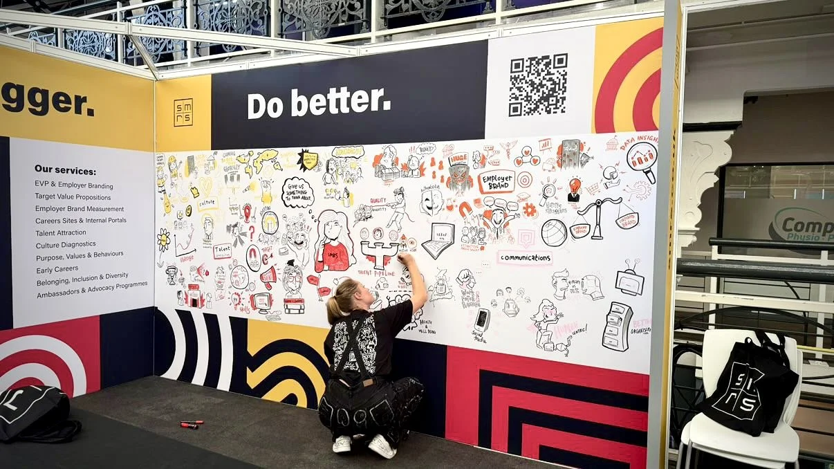 Woman drawing on a large wall display with various sketches and notes at a branding and marketing event.