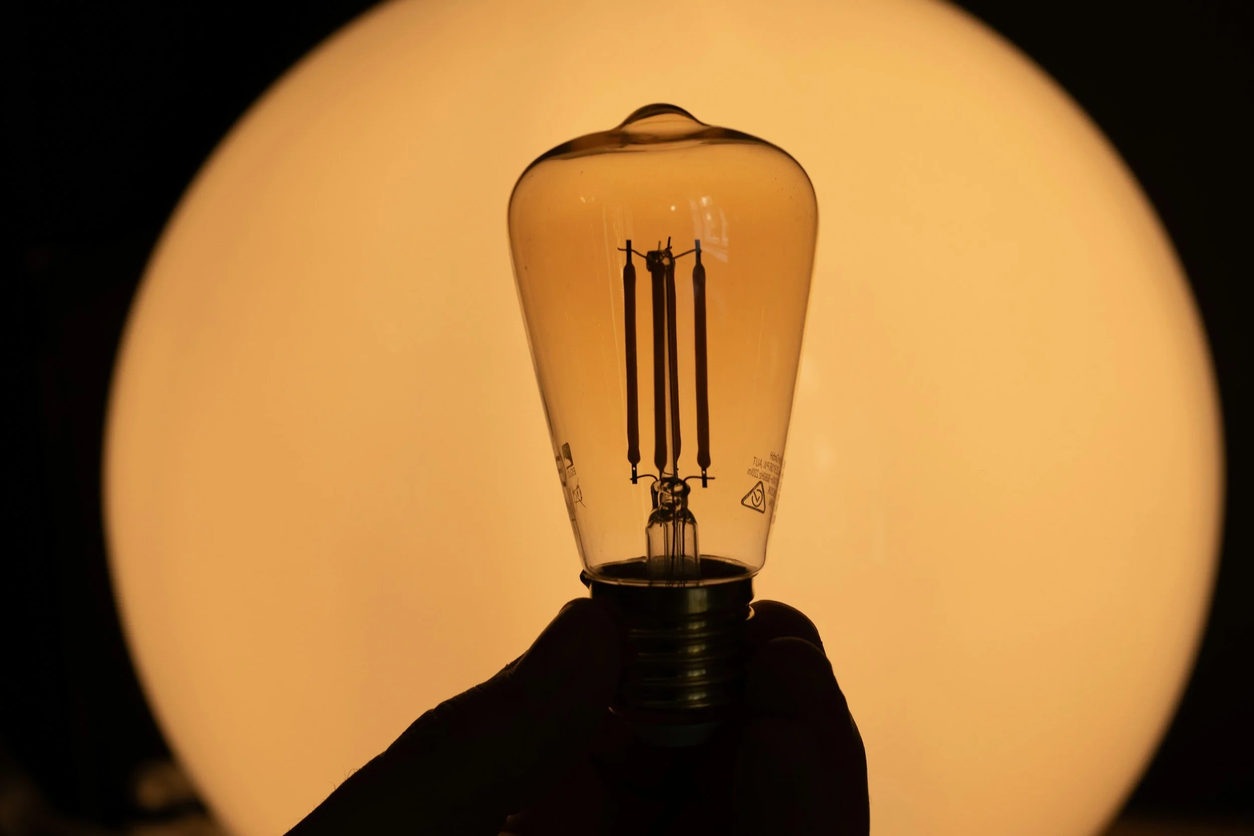 A high contrast, high shadowed hand holds a light bulb against a yellow background, waiting to be lit up with your ideas.