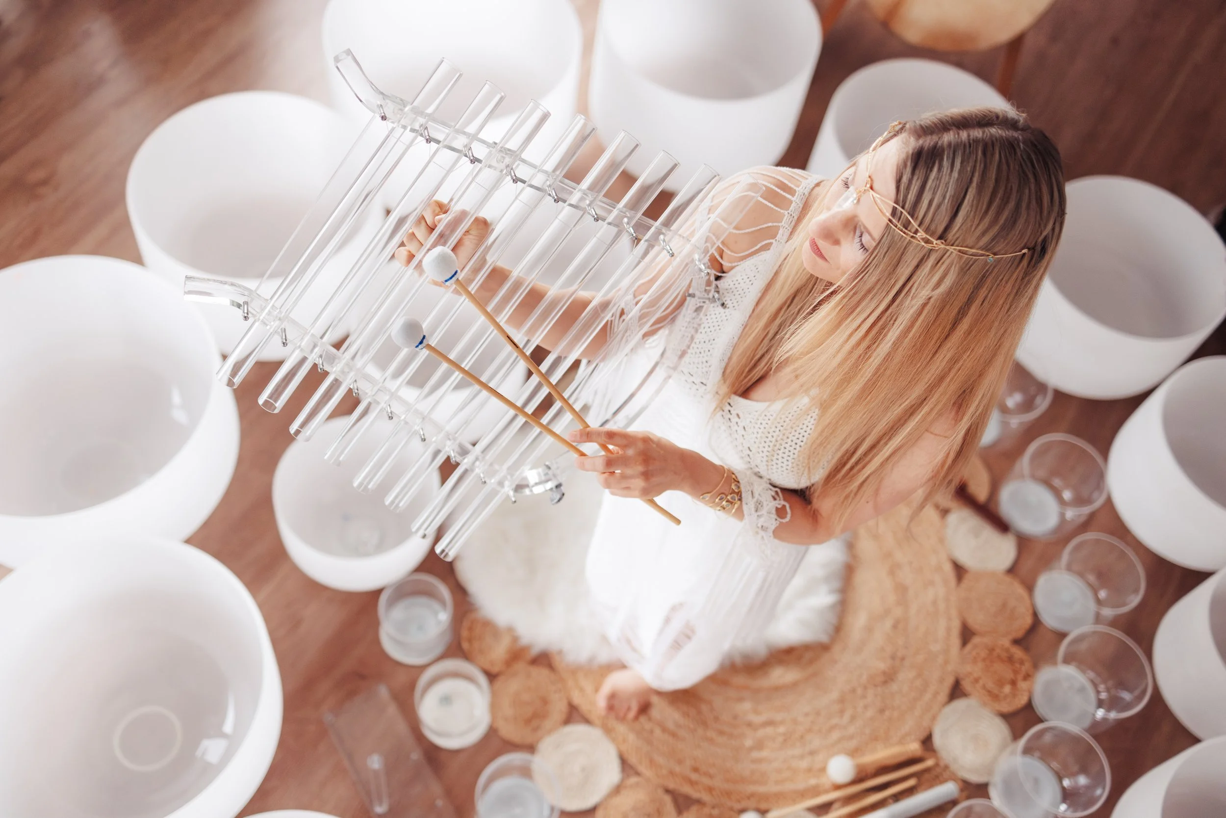 Personne jouant d’un instrument cristallin avec des maillets, entourée de bols de cristal