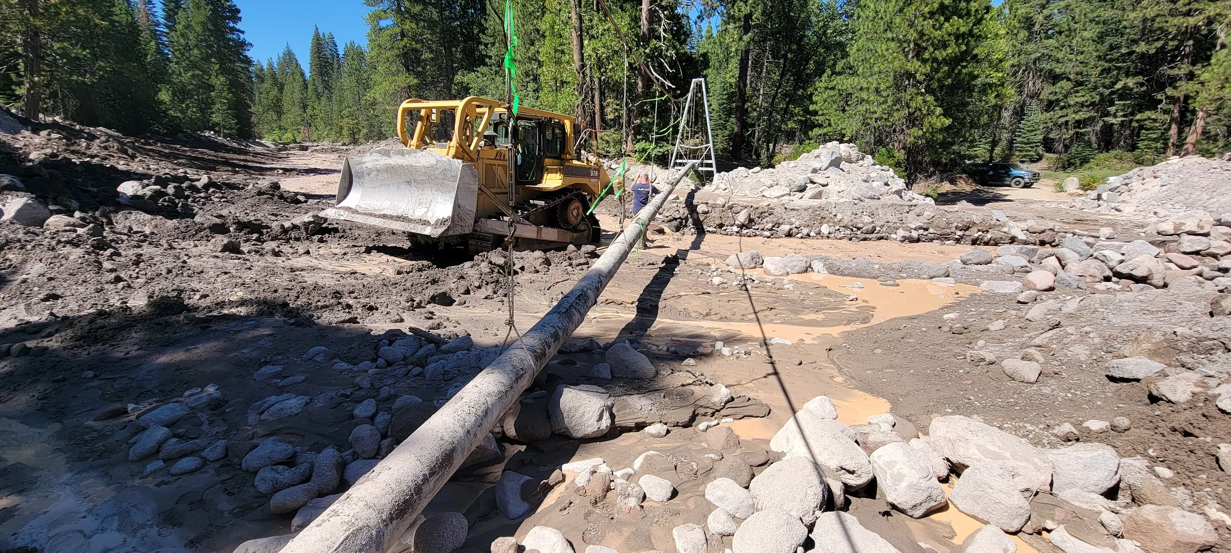 Bulldozer in muddy forest clearing moving large tree log
