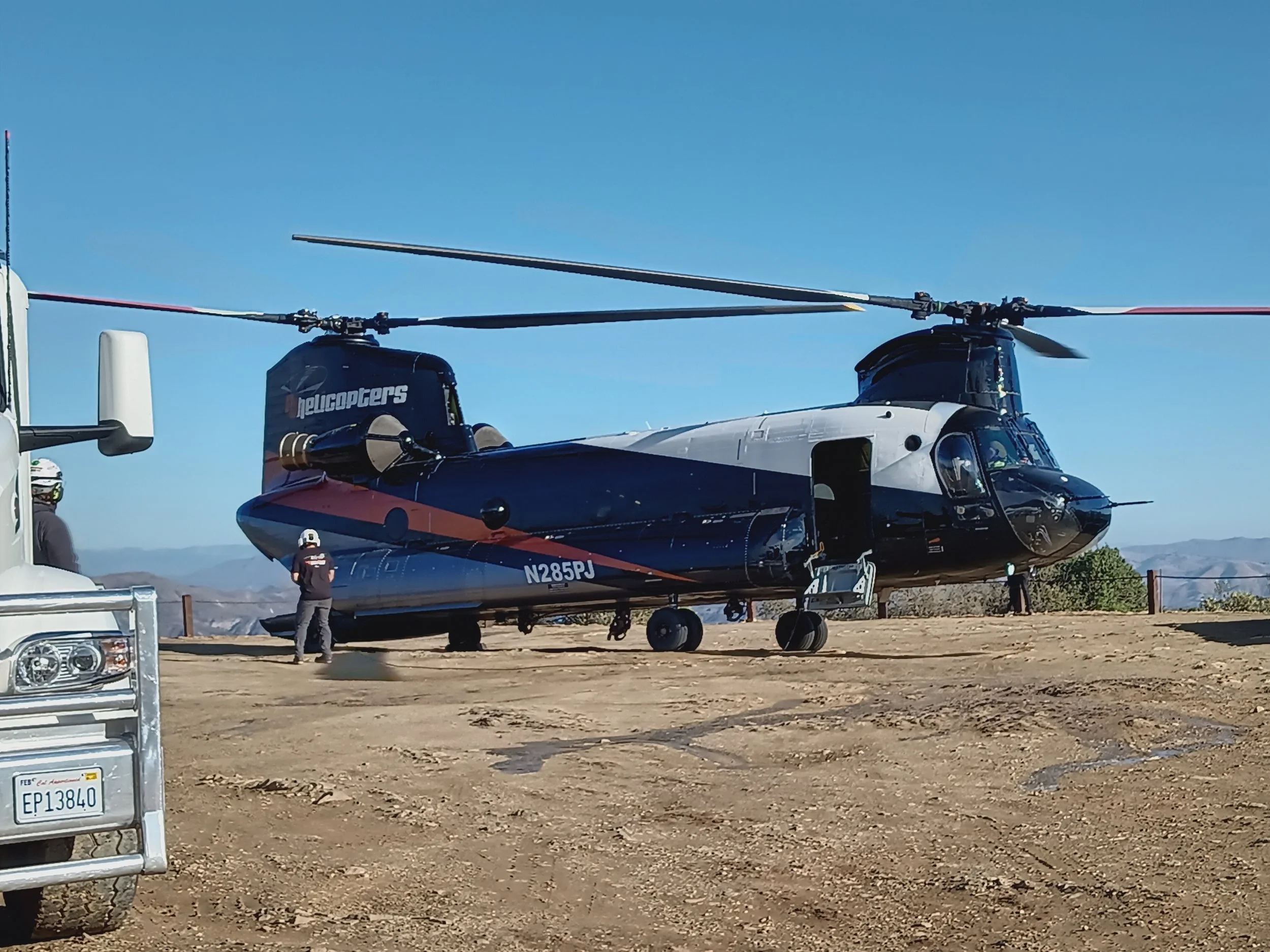 Helicopter on dirt surface next to service truck with personnel