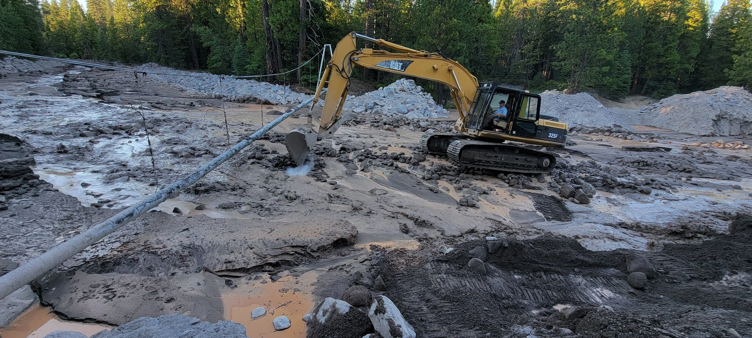 Excavator working on muddy construction site with pipeline and forest background